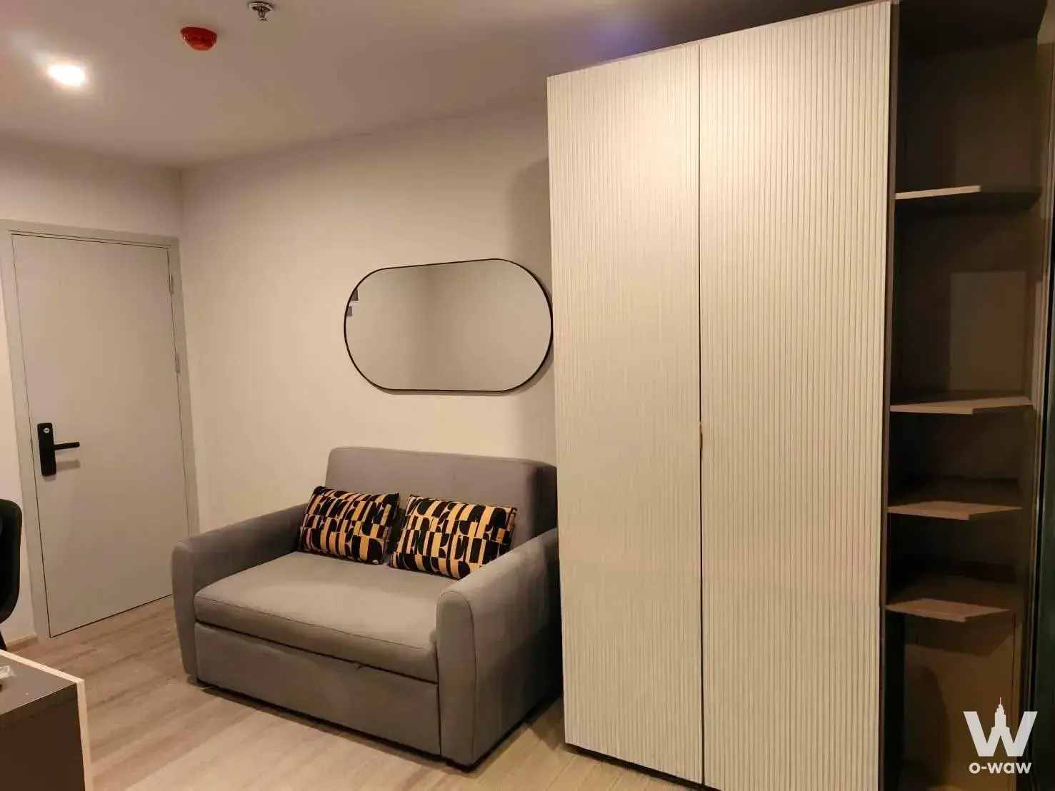 Minimalist studio living space with grey sofa bed, white wardrobe, and light beige flooring