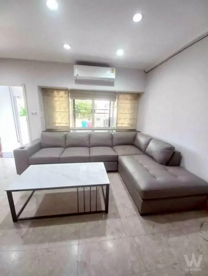 Modern living room in 3-bed Baan Klang Mueang townhouse with grey sectional sofa and marble-tiled floor