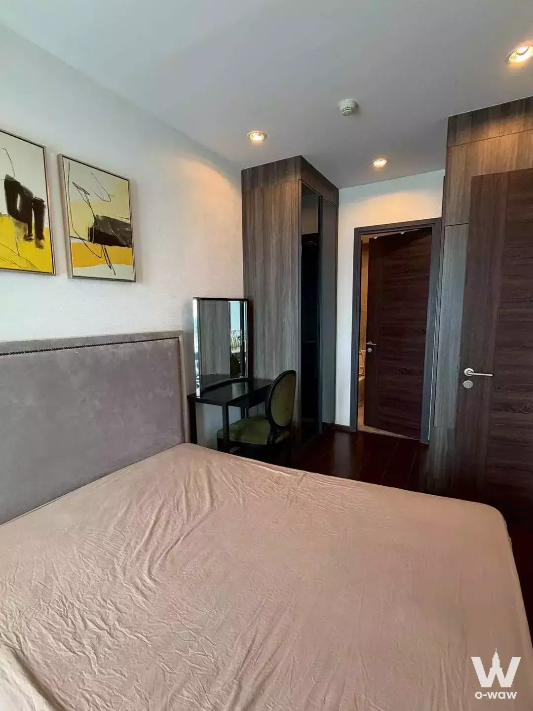 Modern bedroom in 1-bed C Ekkamai condo for rent featuring grey bed, dark wood floors, and abstract art