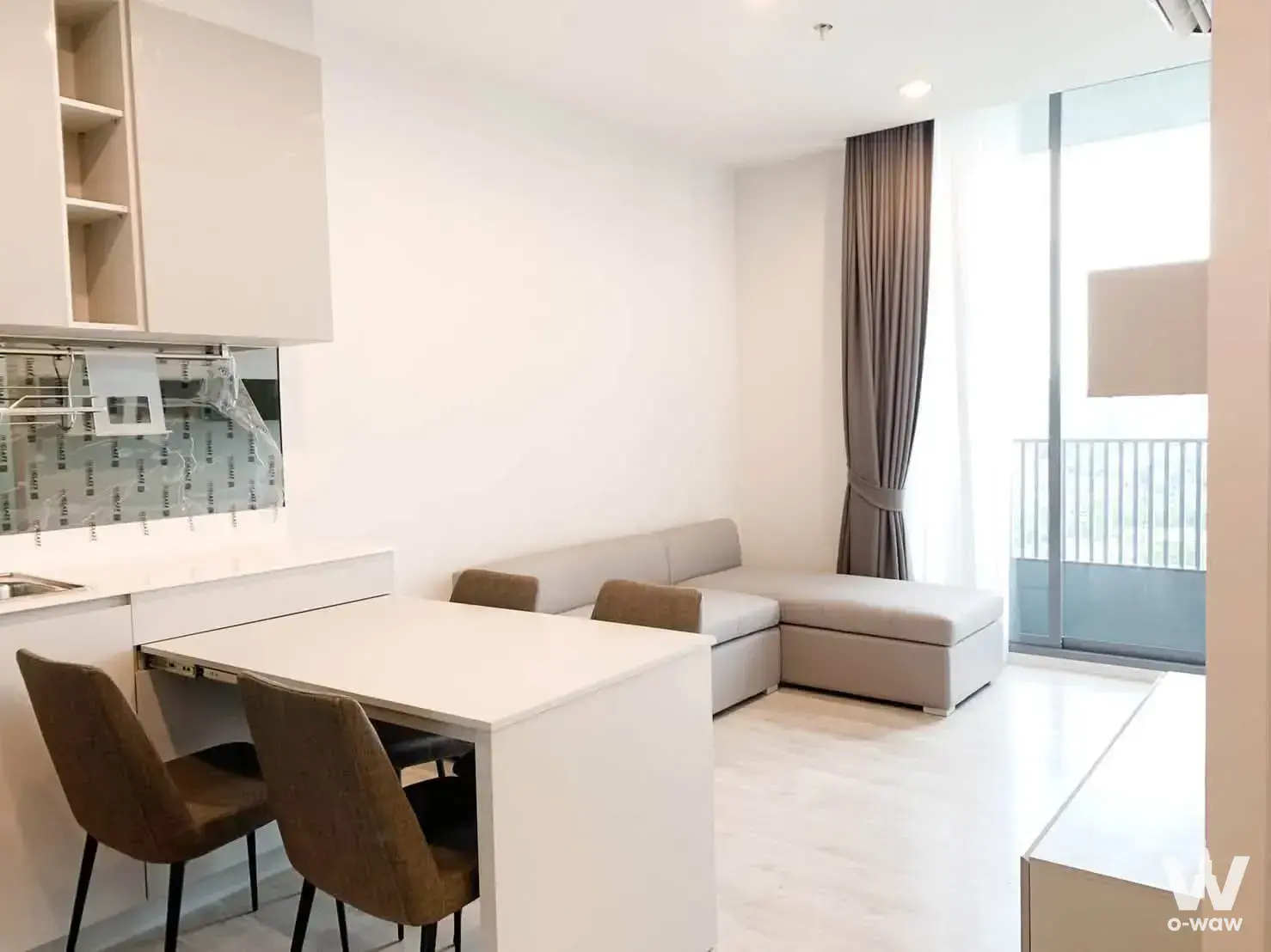 Open-plan condo living and dining space with beige sofa, extendable table, and balcony access