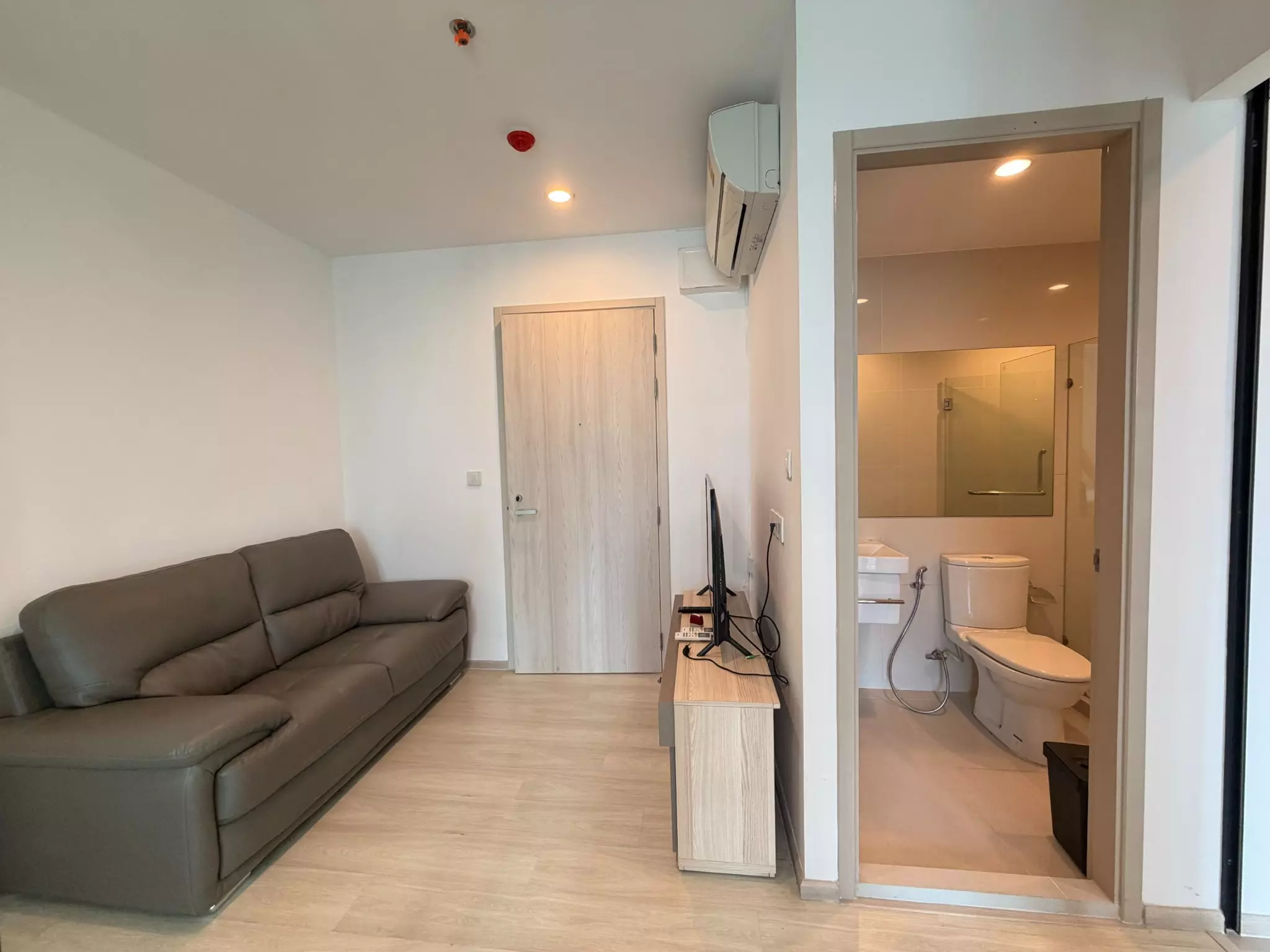 Modern 1-bed condo for rent in Life Asoke featuring a brown leather sofa and open-plan bathroom