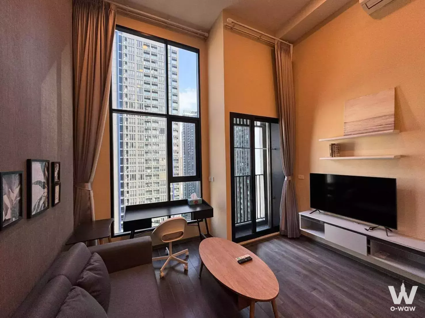 Modern living room with yellow accent walls, grey sofa, and floor-to-ceiling windows in KnightsBridge Space Rama 9 condo