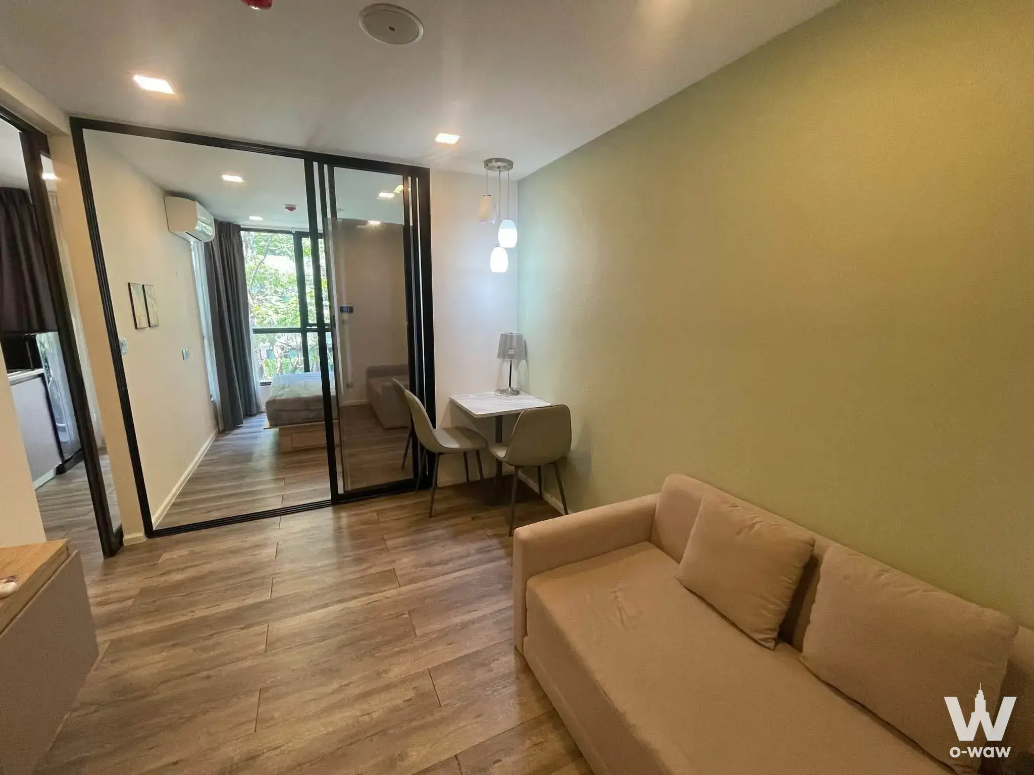 Bright living area with sage walls, beige sofa, and dining set in 2-bed condo for rent at Atmoz Ratchada Huai Khwang
