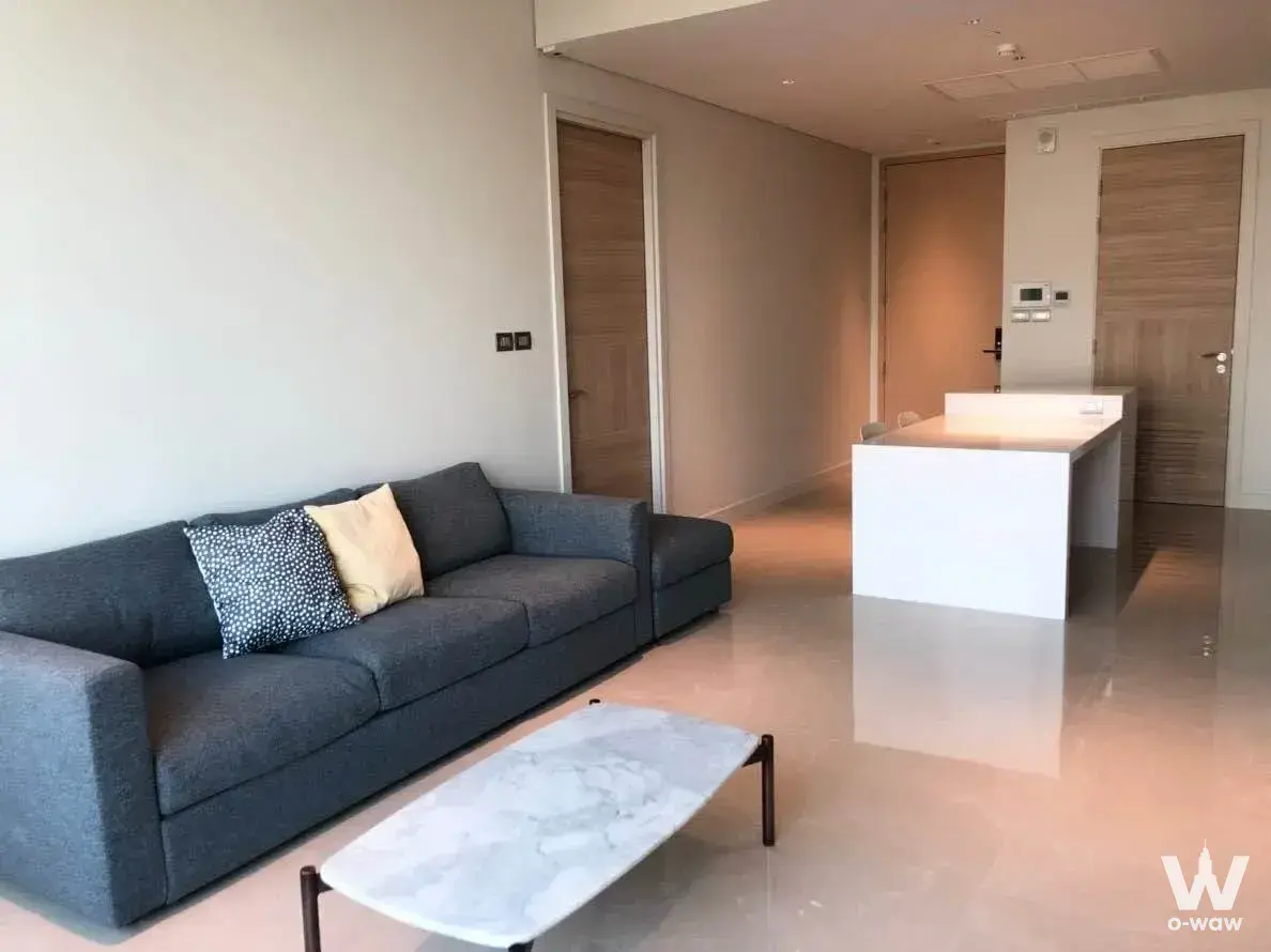 Modern 1-bed condo for rent in Sindhorn Residence featuring grey sectional sofa and marble coffee table on glossy beige tiles