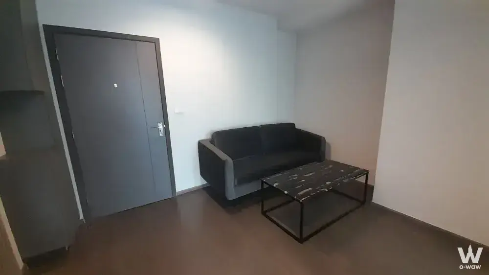 Minimalist living room with dark laminate floors and black sofa in 1-bed condo for rent at Ideo Sukhumvit 93