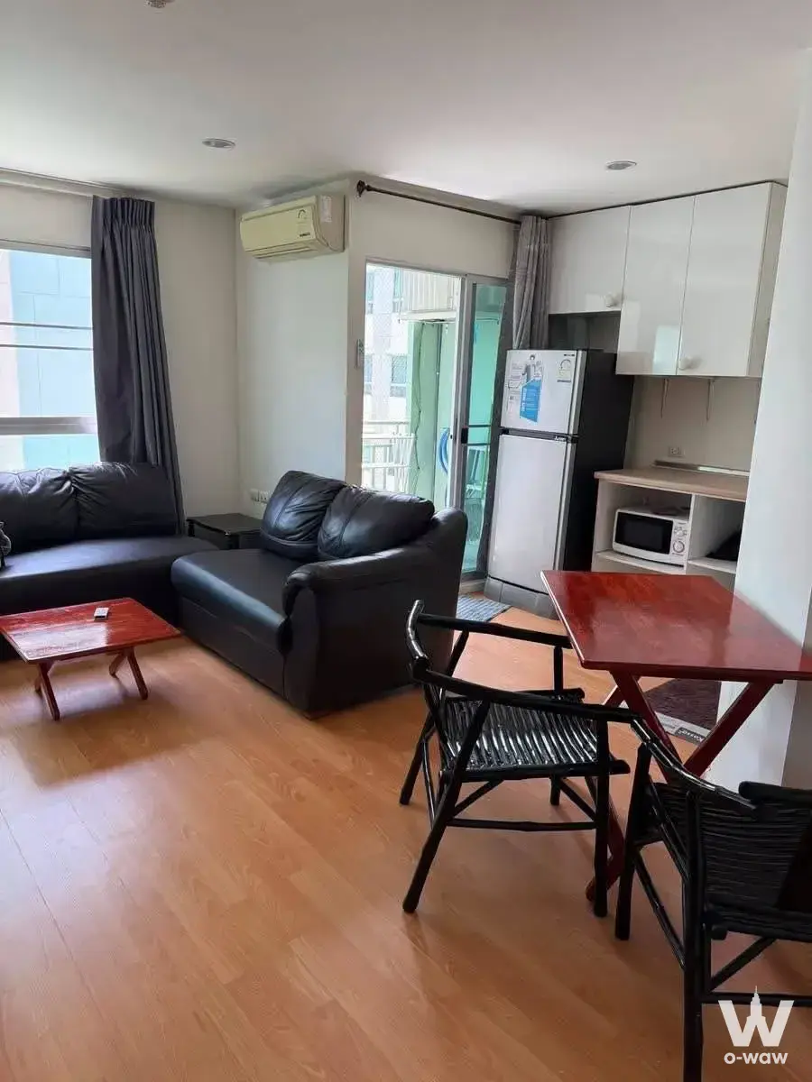 Spacious living room in Lumpini Ville On Nut condo with black leather sofas, open kitchen, and balcony access
