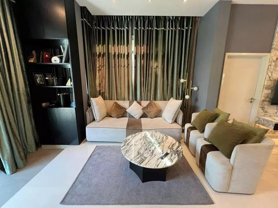 Modern living room in 4-bed Bangkok condo for sale featuring olive green accents, beige sofa, and marble coffee table