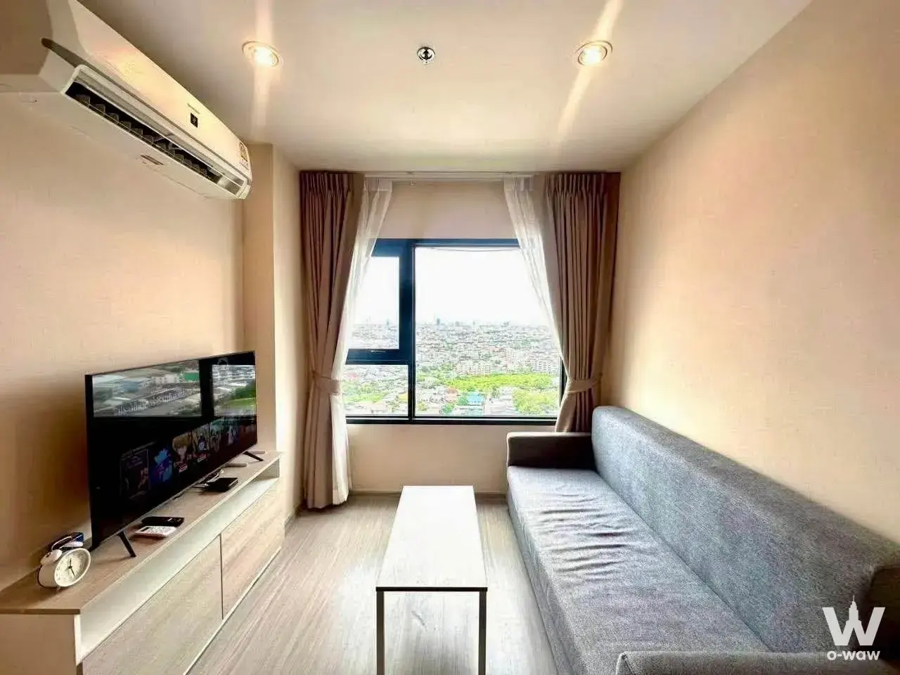 Living room in Aspire Erawan Prime 2-bed condo featuring a city skyline view and light-grey sofa