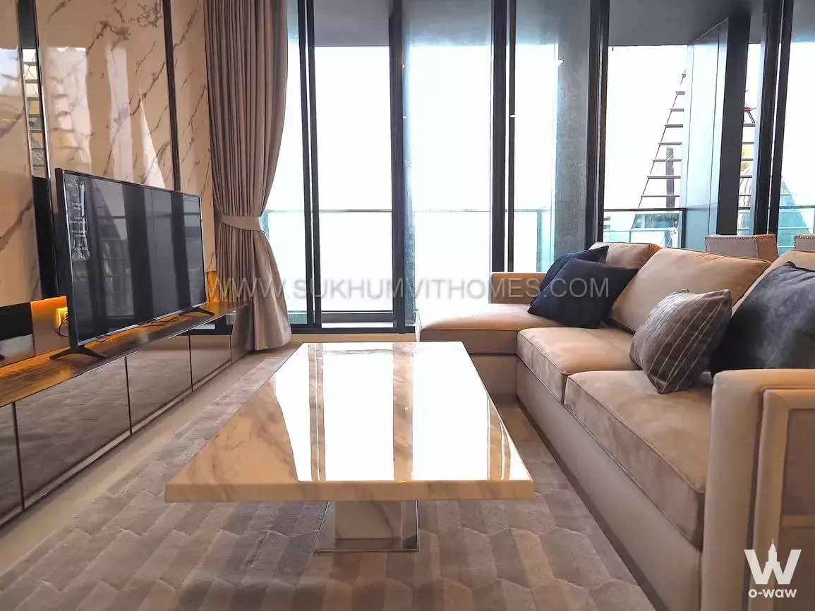 Bright living room with floor-to-ceiling windows and beige sectional sofa in 2-bed condo for rent at Noble Ploenchit