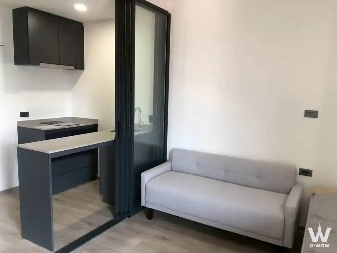 Compact studio in Groove Scape Ladprao-Sutthisan with dark grey kitchenette cabinets and a light grey fabric two-seater sofa