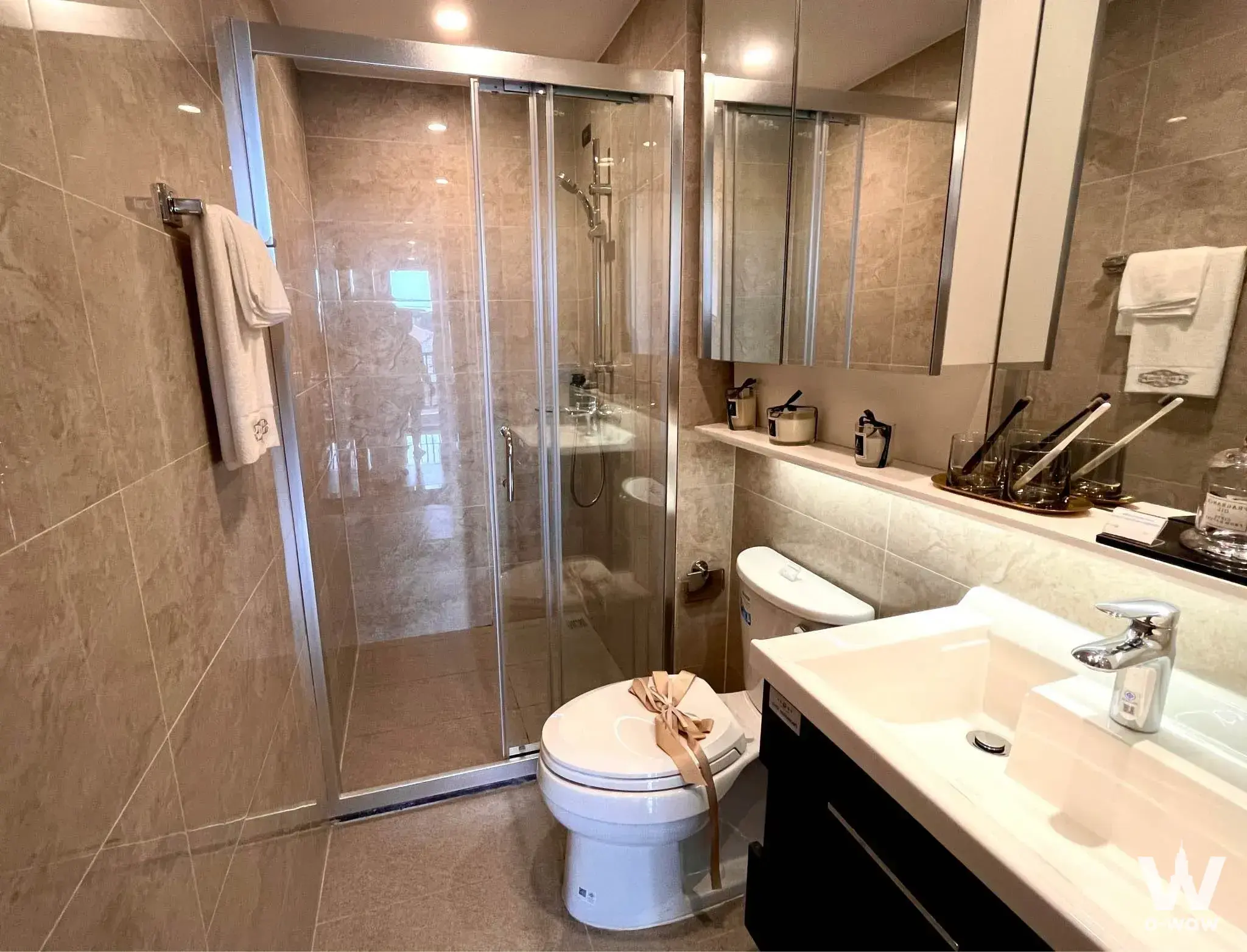 Modern bathroom in Regal Srinakarin 40 featuring beige tiles, glass shower enclosure, and black vanity