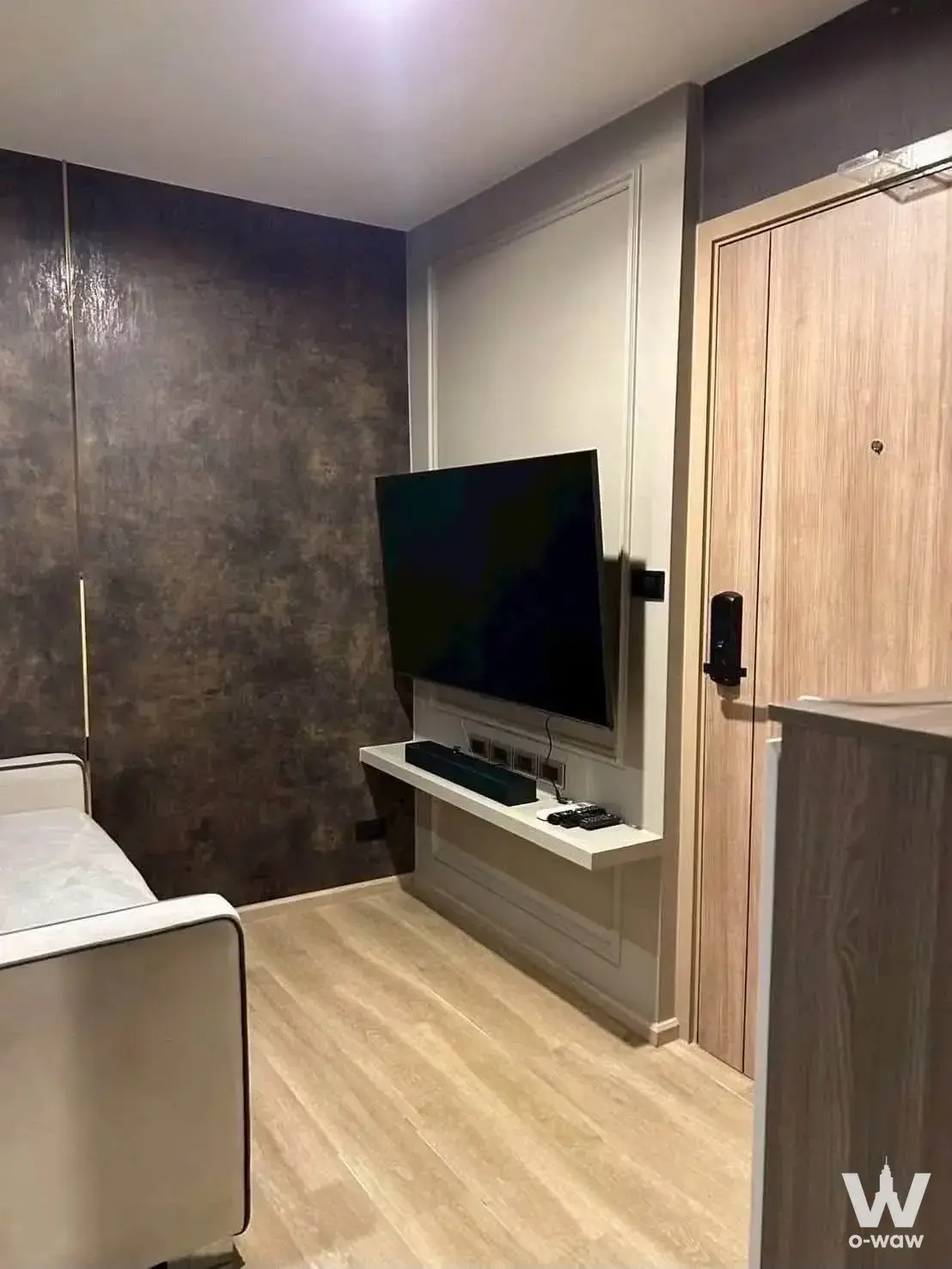 Living room in The Excel Hideaway Sukhumvit 50 with mounted TV, floating shelf, and smart lock door
