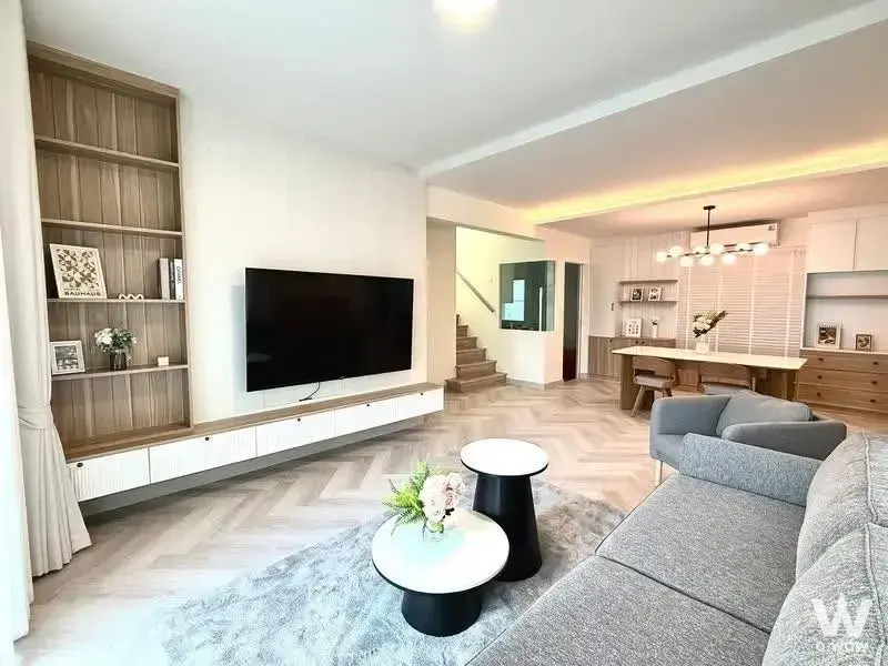 Spacious open-plan living room in Villaggio 3 Srinakarin-Bangna with herringbone floors, grey sectional, and staircase