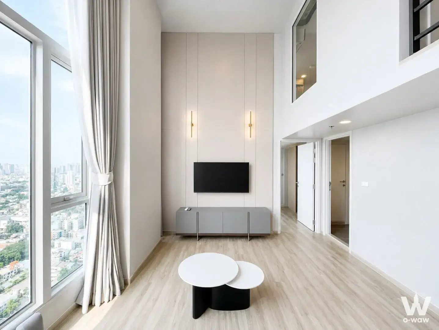 High-ceiling living room in Culture Thonglor duplex with mezzanine, gold sconces, and city view