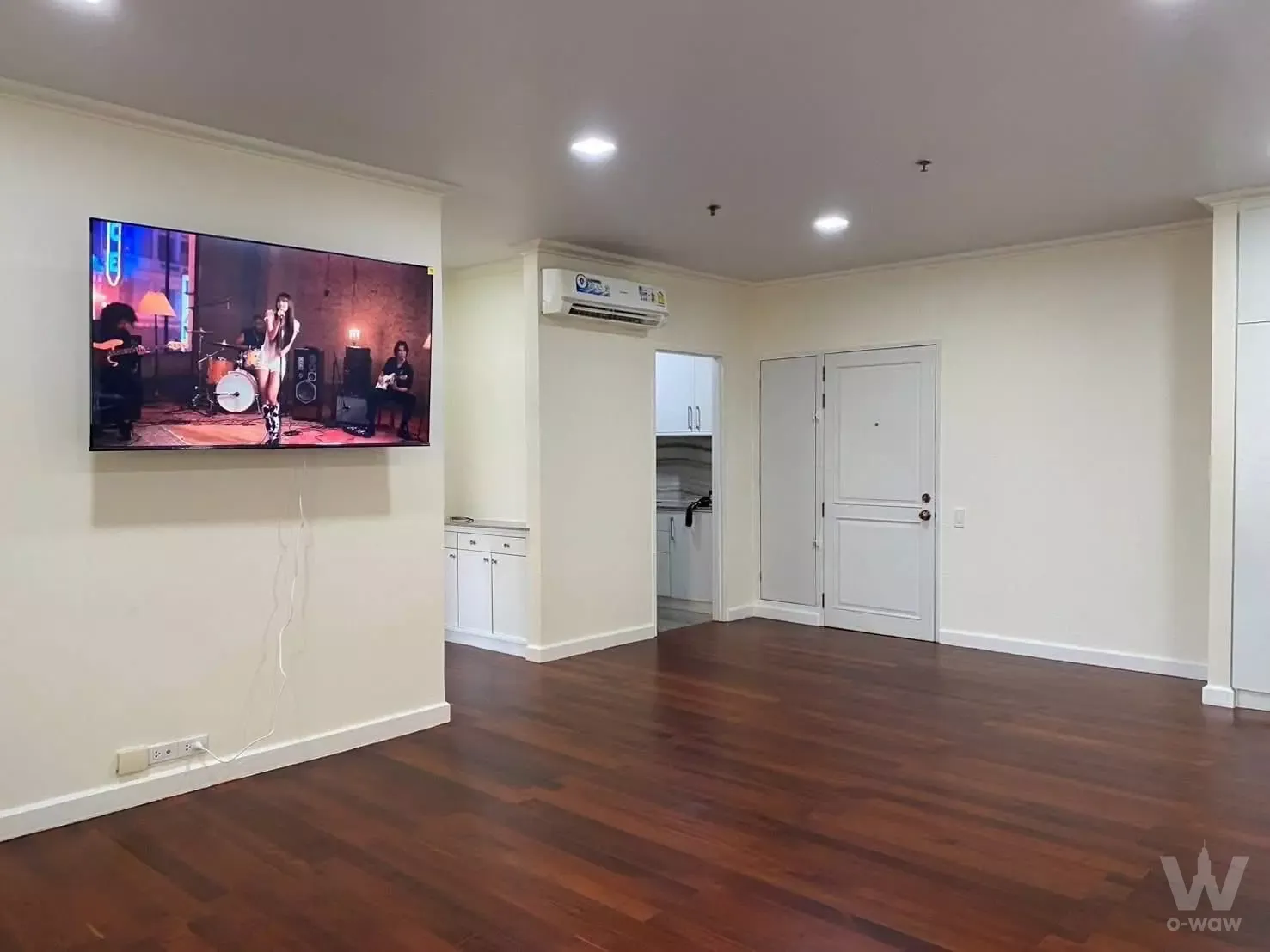 Empty living room in Baan Chaopraya 1-bed condo for sale with dark wood floors and wall-mounted TV