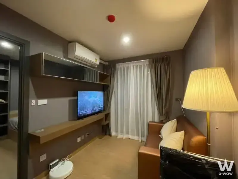Taupe living room with dark wood TV unit and brown leather sofa in Asher Ratchada-Huaikhwang 1-bed condo