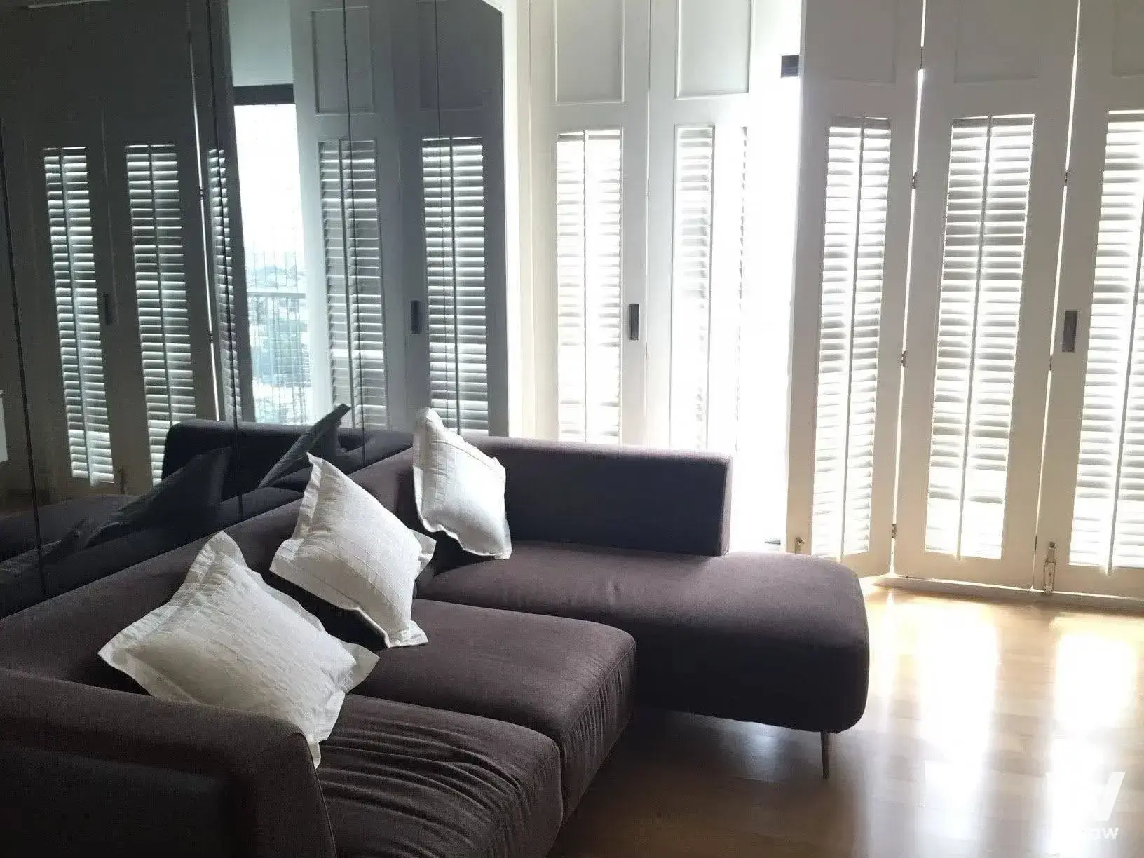 Modern condo living room with charcoal sectional sofa and floor-to-ceiling mirrored wardrobe panels