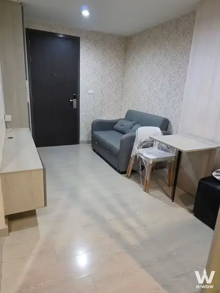 Compact studio living space with grey sofa and floral wallpaper in 1-bed condo for sale at Niche ID Sukhumvit 113