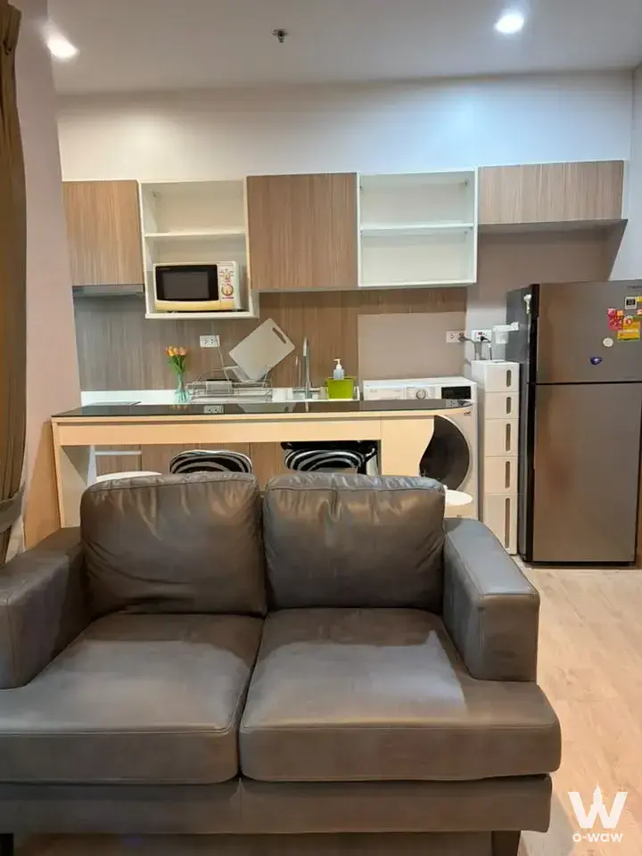 Open-plan studio living area with dark grey sofa and wood floors in The Parkland Phet Kasem-Tha Phra condo