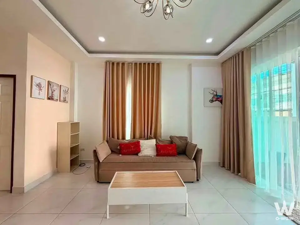 Bright living room with beige sofa and botanical prints in a 2-bed house for rent in หมู่บ้านรัตนากรวิลเลจ 17