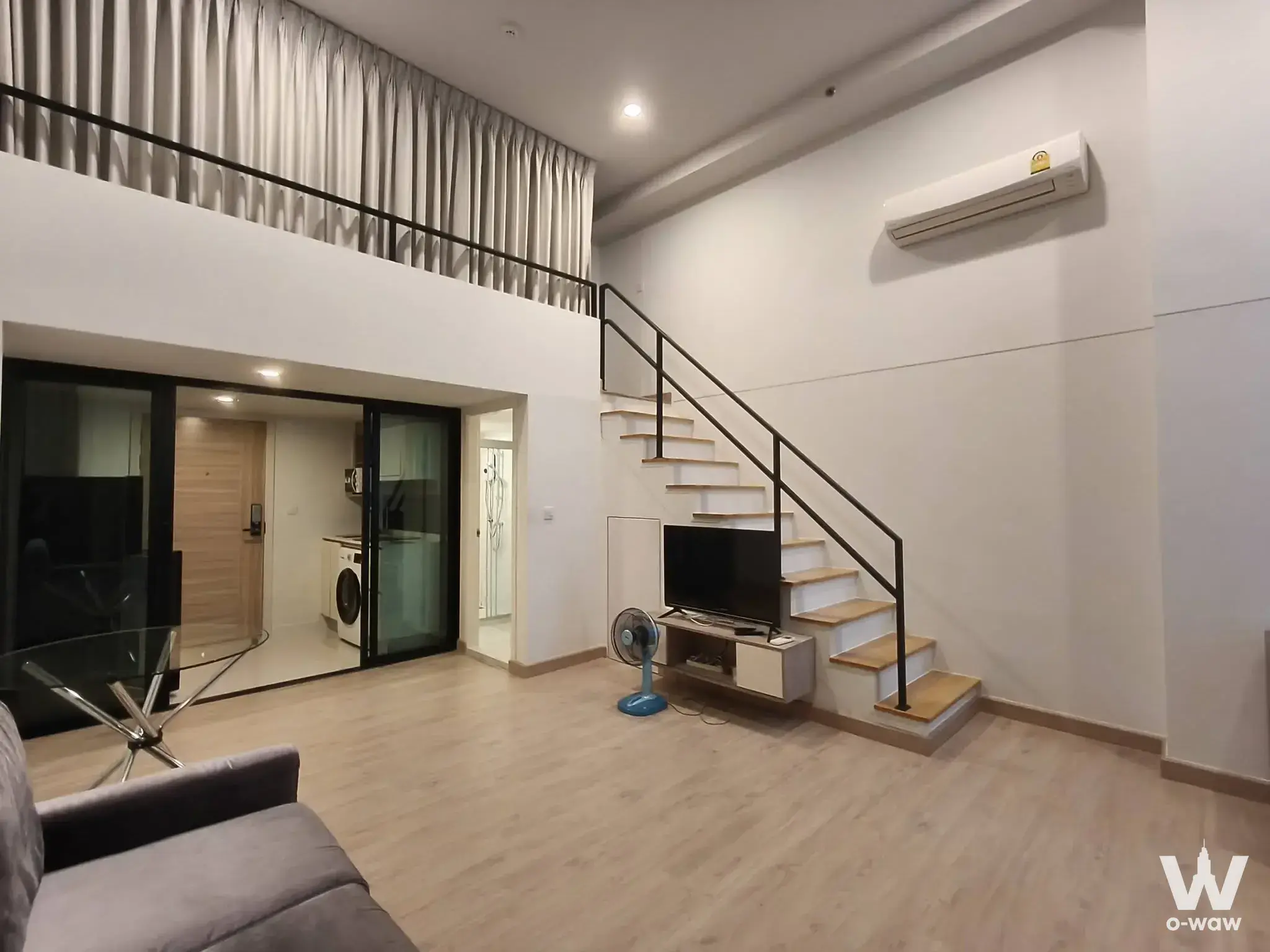Double-height living room in a Knightsbridge Duplex Tiwanon condo with light wood floors and open staircase