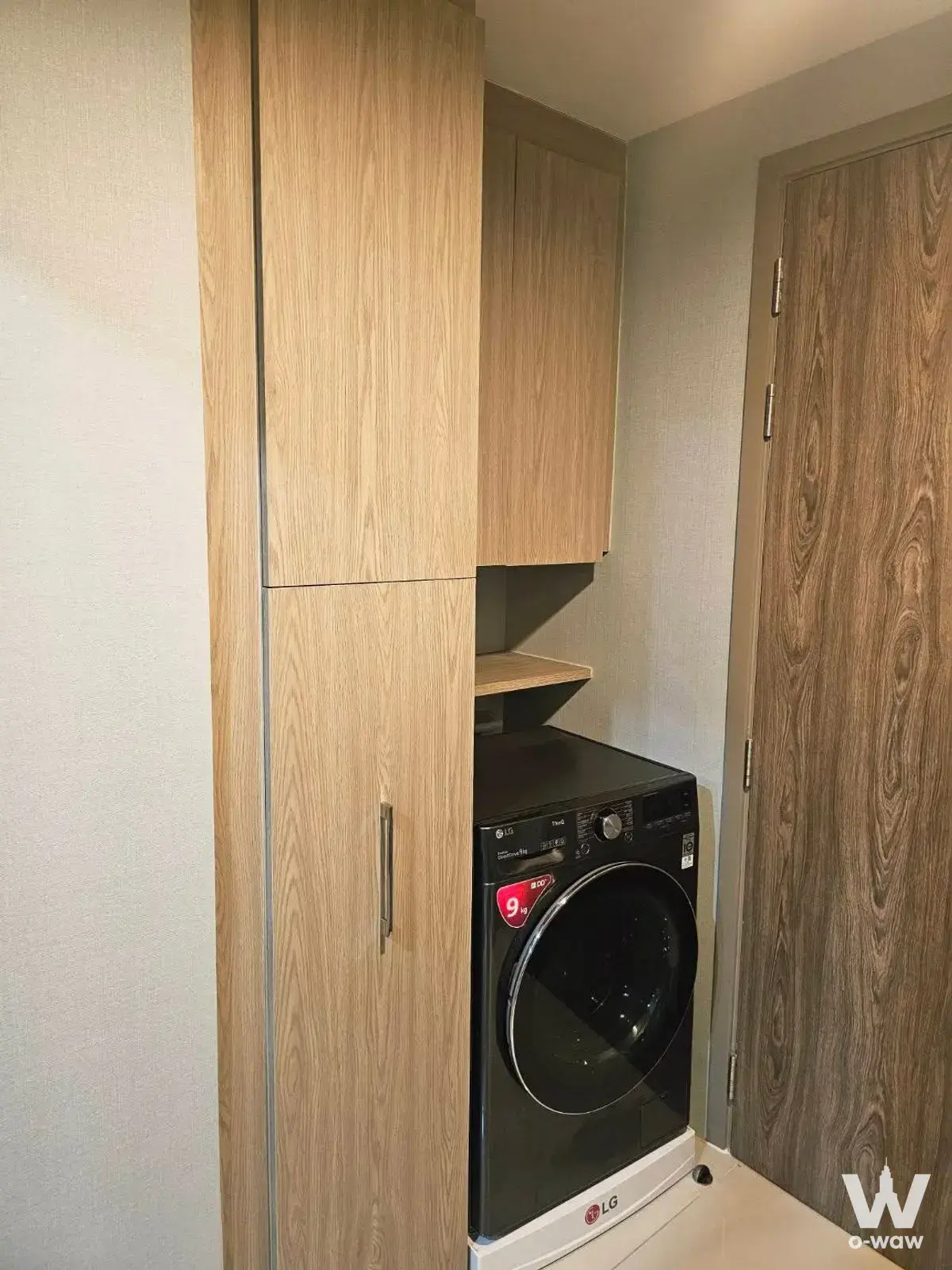 Compact laundry nook in Niche MONO Sukhumvit Bearing unit featuring LG washer and light oak built-in cabinetry