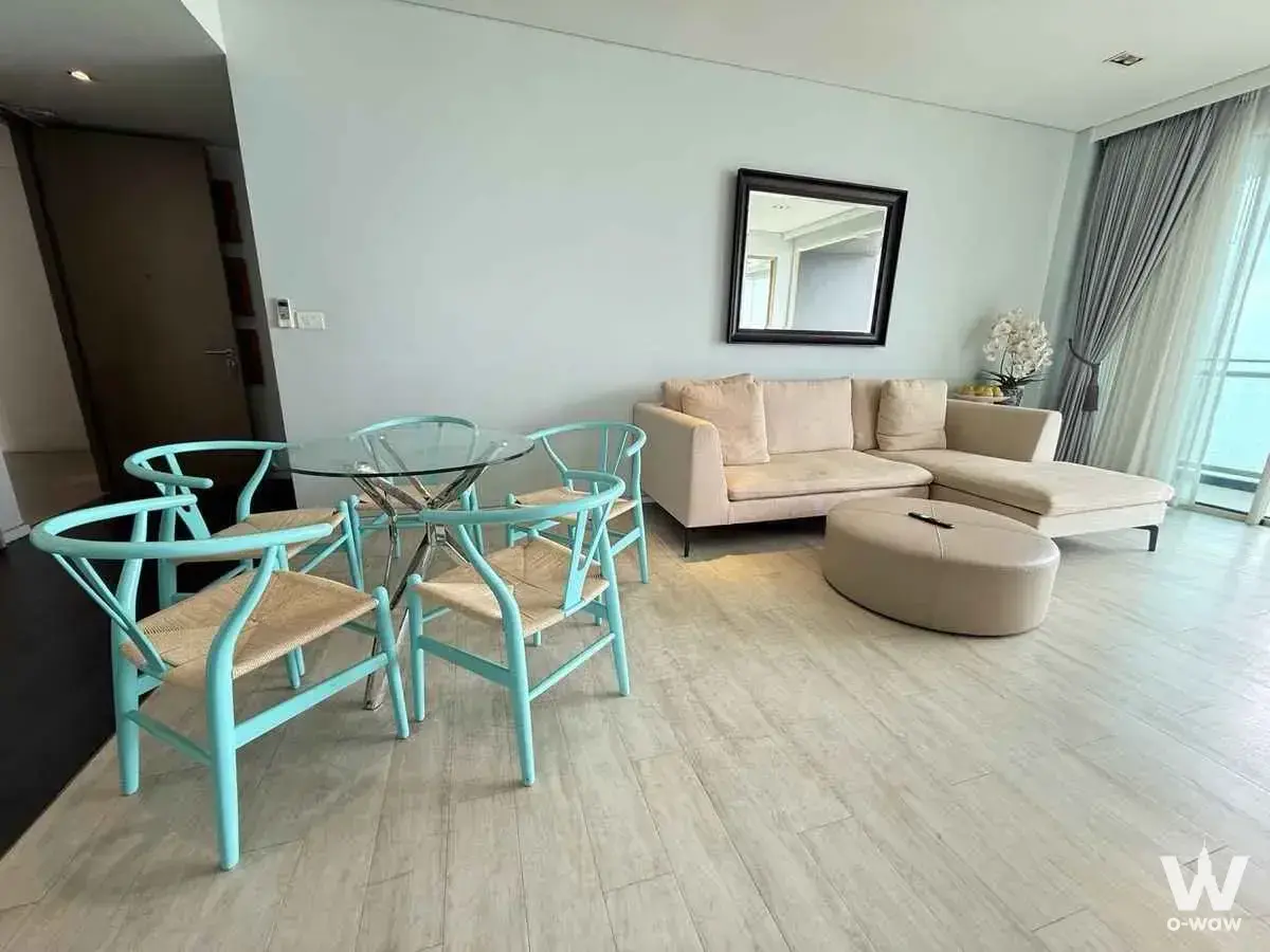 Living room with beige sectional sofa, turquoise Wishbone chairs, and glass-top dining table near balcony