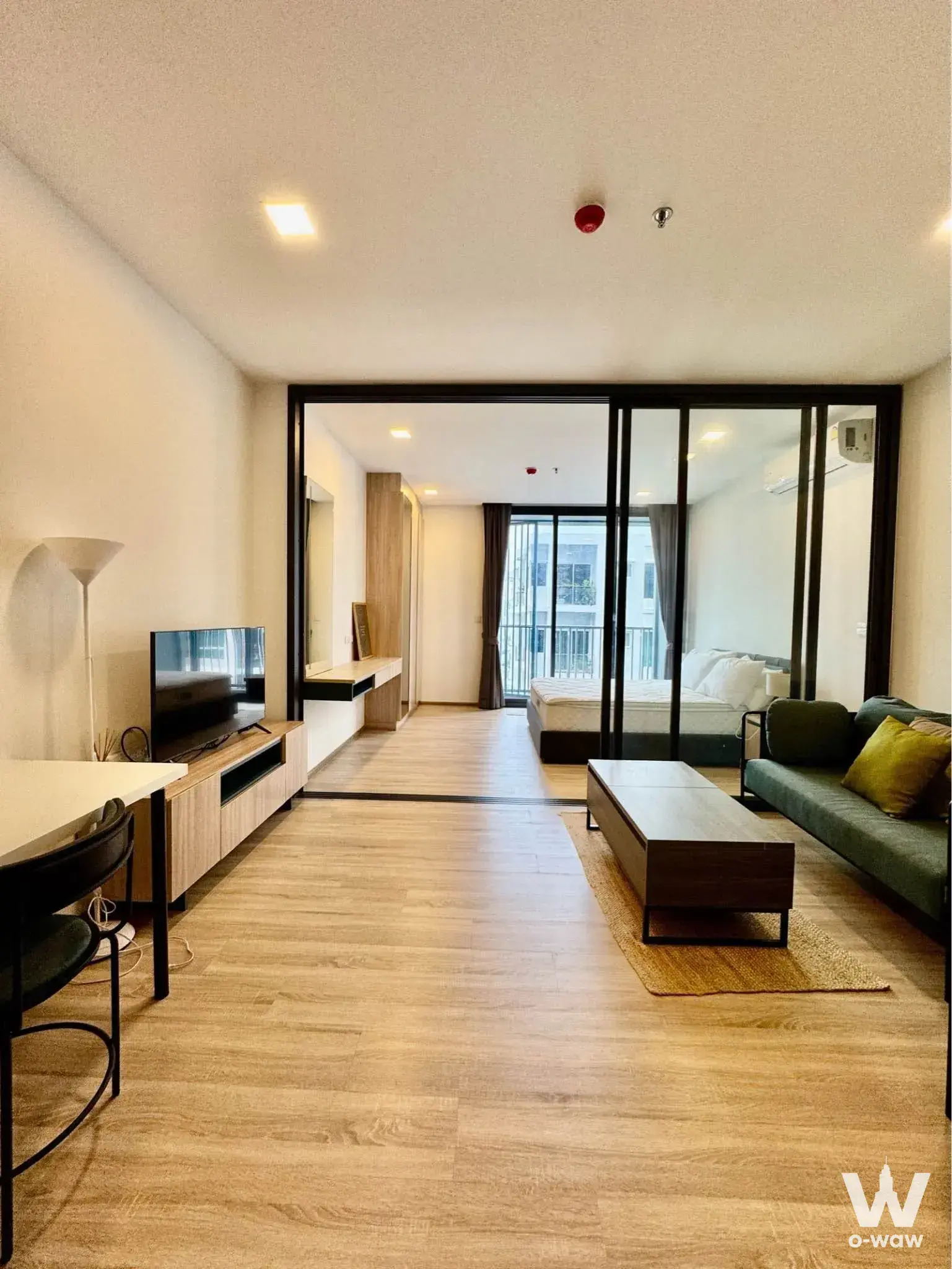 Open-plan living room in XT Phayathai with green sofa, glass partition, and oak flooring