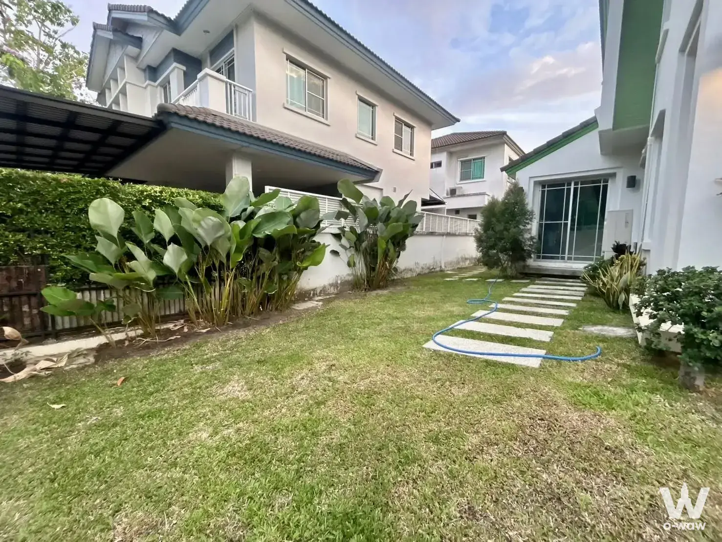 Mantana Onnut-Wongwaen 3 house rear garden with green lawn, stone path, and tropical plants near beige home