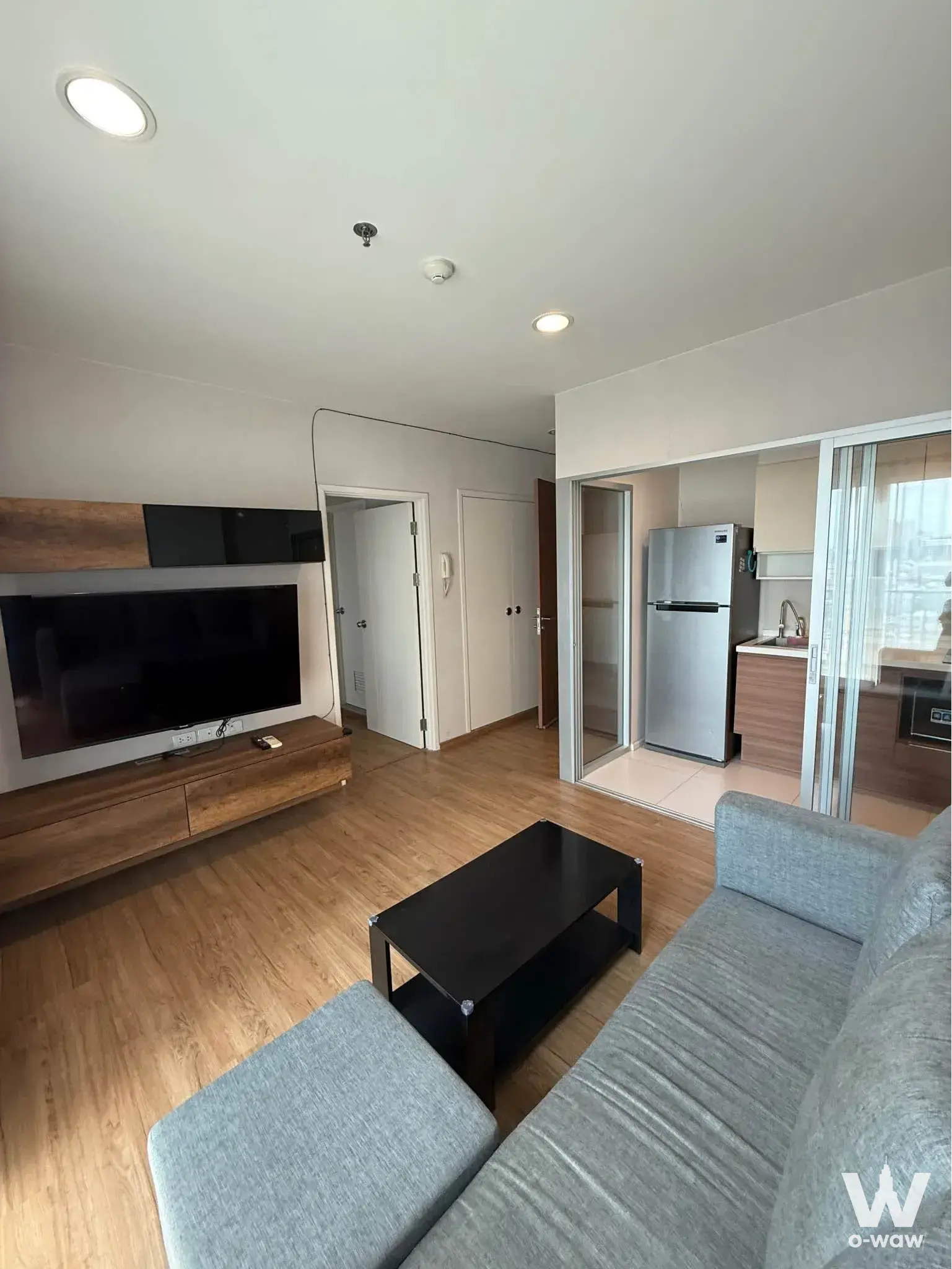 Open-plan living room in a Fuse Chan Sathorn condo with grey sofa and wall-mounted TV