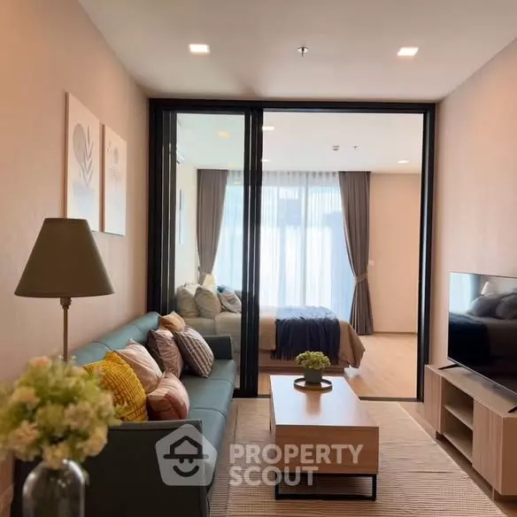 Open-plan living room in XT Phayathai condo featuring teal sofa, sliding glass doors to bedroom, and light wood floors
