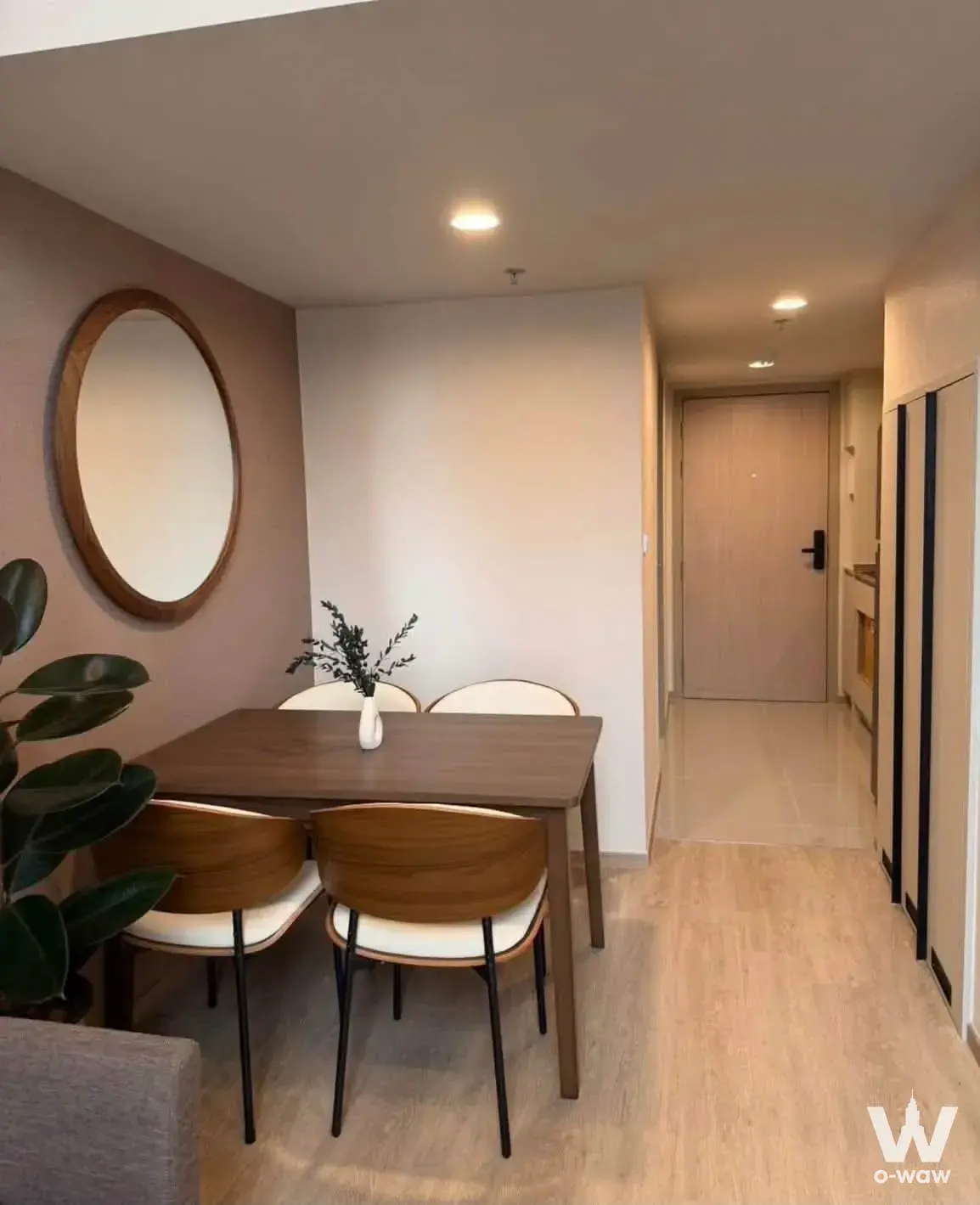 Dining area with dark wood table, dusty-rose accent wall, and rubber plant in Culture Chula condo for rent
