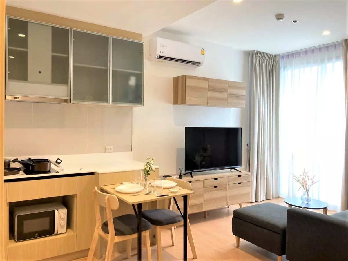 Open-plan living and kitchenette in MARU Ekkamai 2 condo with light wood cabinetry and floor-to-ceiling windows