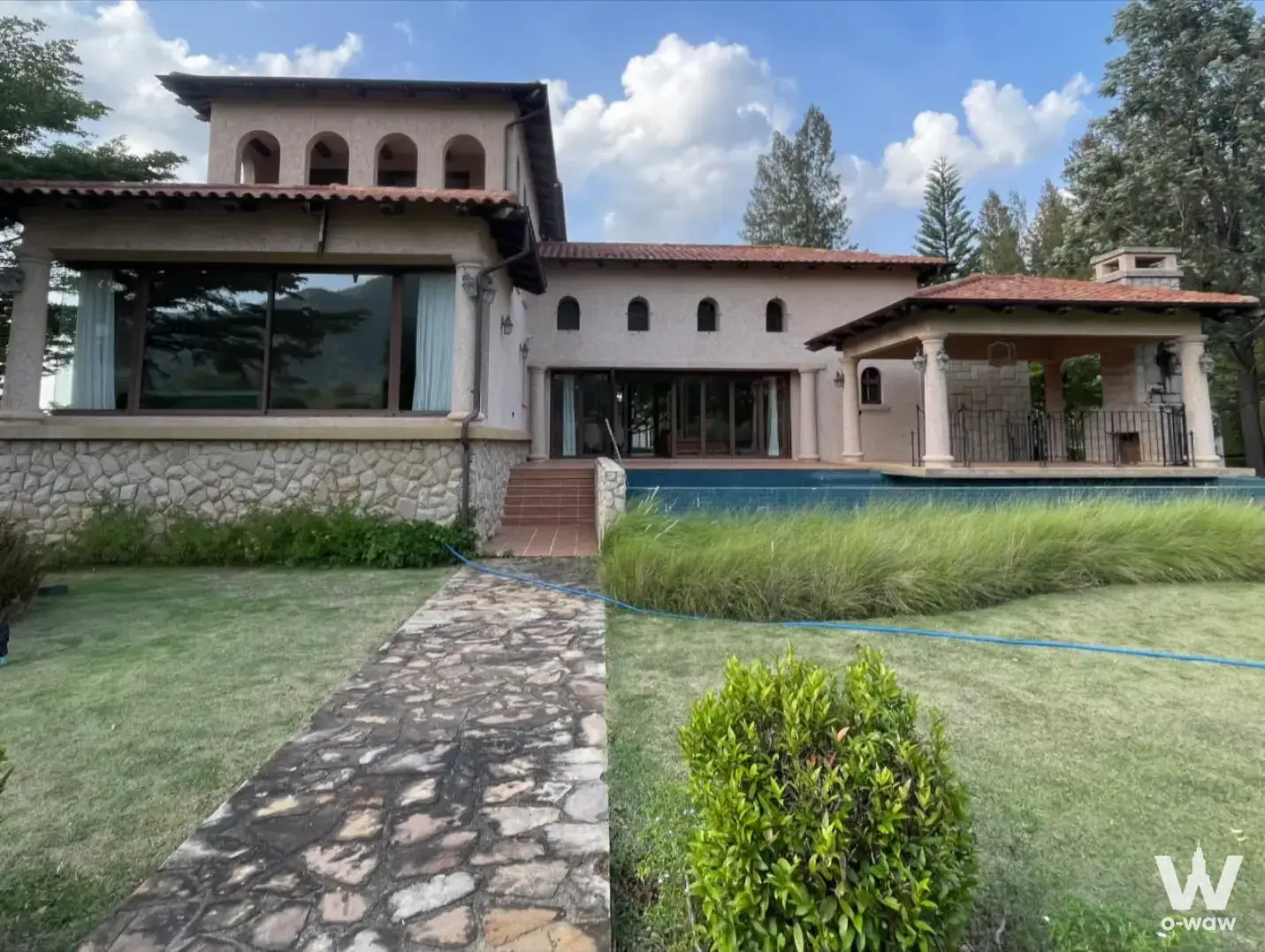 Two-story Mediterranean villa with beige stucco walls, terracotta roof, swimming pool, and manicured lawn