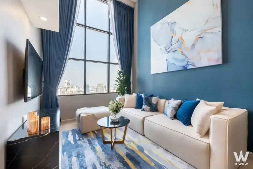 Living room in a KnightsBridge Prime Sathon condo with a cream sofa teal accent wall and city skyline view