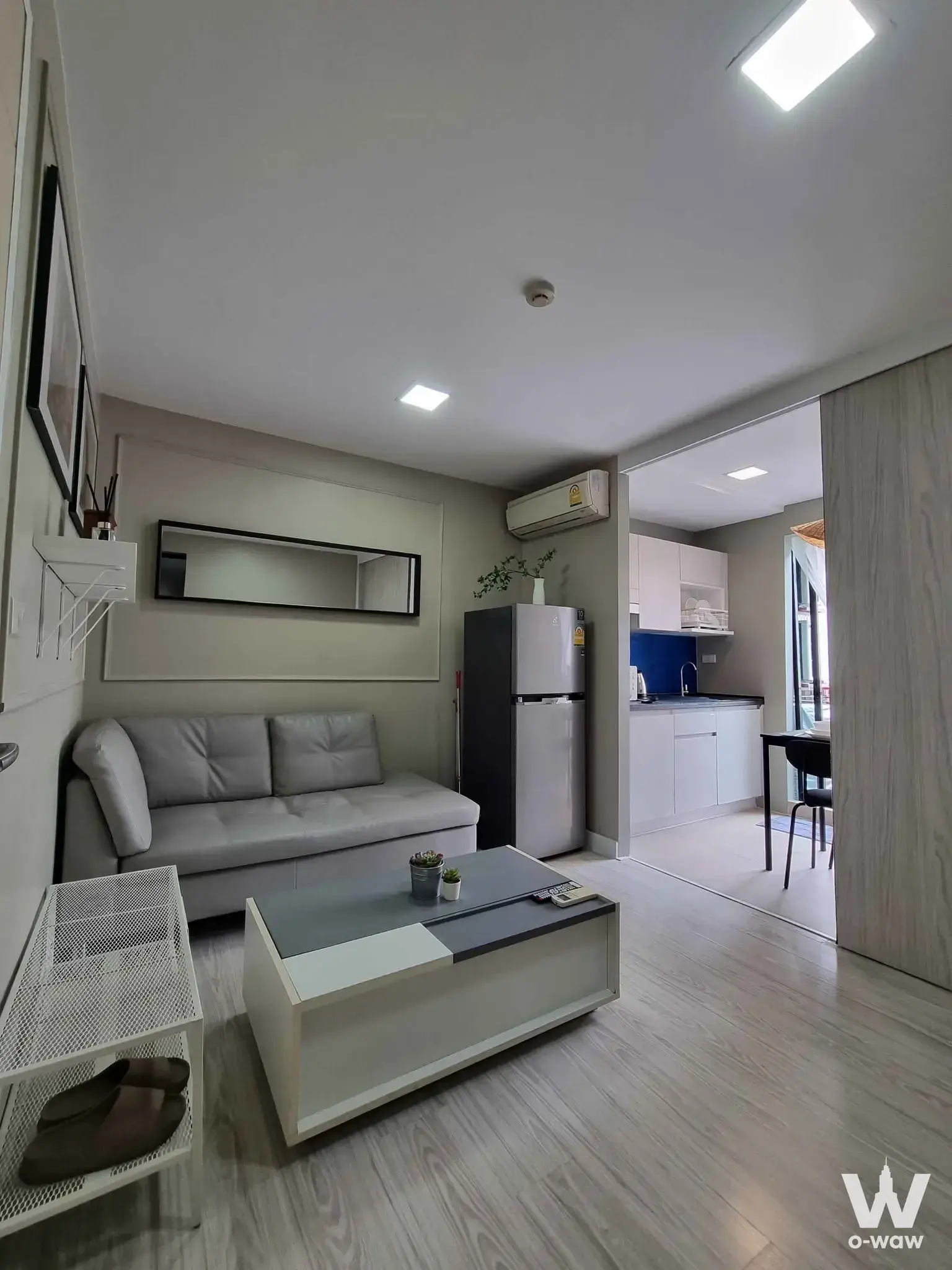 Open-plan studio in a 1-bed rental condo at Mestyle Sukhumvit Bang Na has a grey sofa and dark blue kitchen backsplash