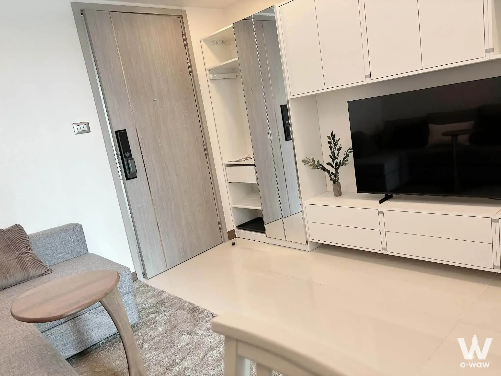 Minimalist living room with glossy white tiles, grey sofa, open wardrobe, smart lock door, and built-in entertainment unit
