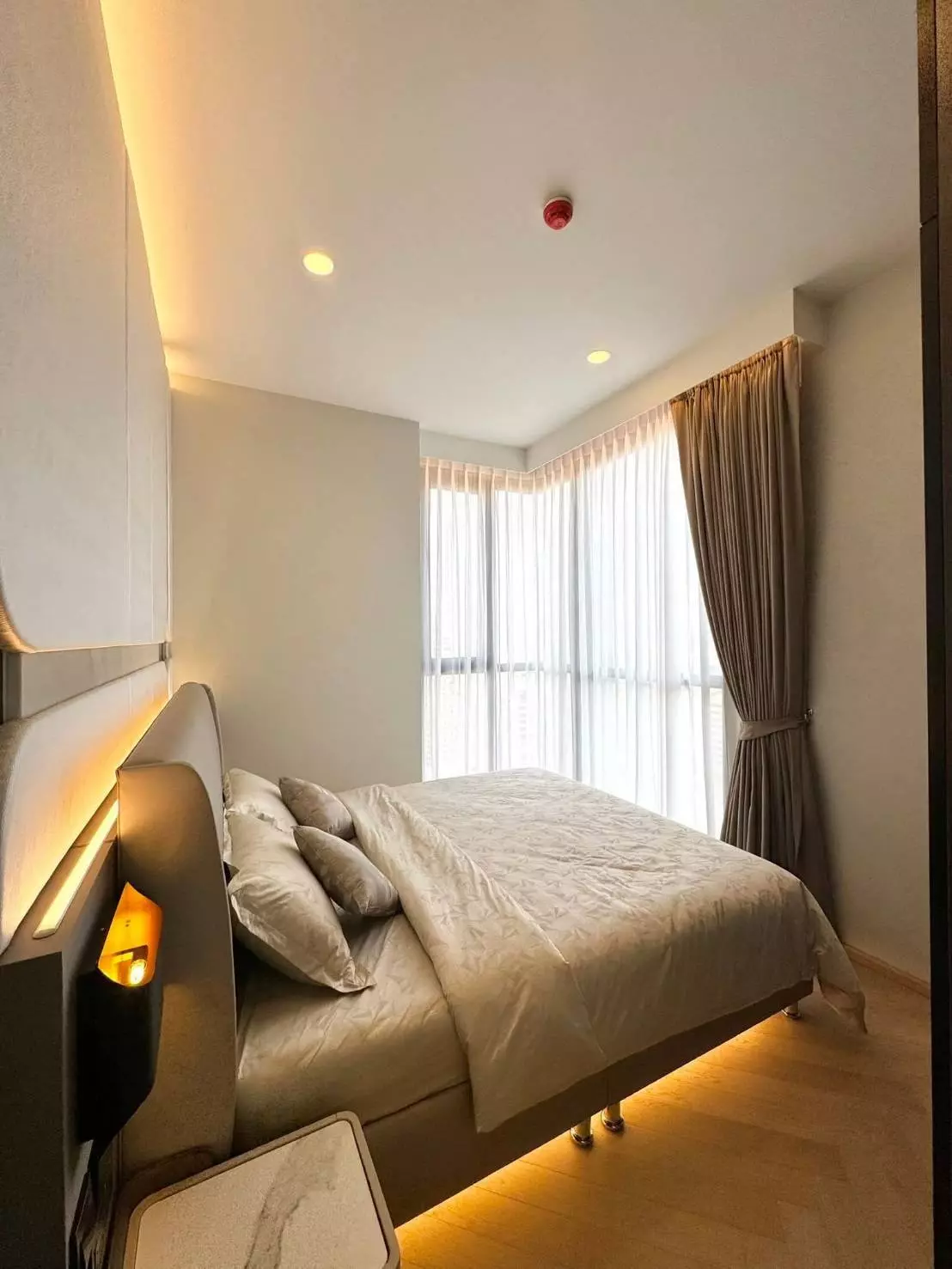 Minimalist bedroom with taupe upholstered bed, cove lighting, and sheer curtains in Park Origin Thonglor