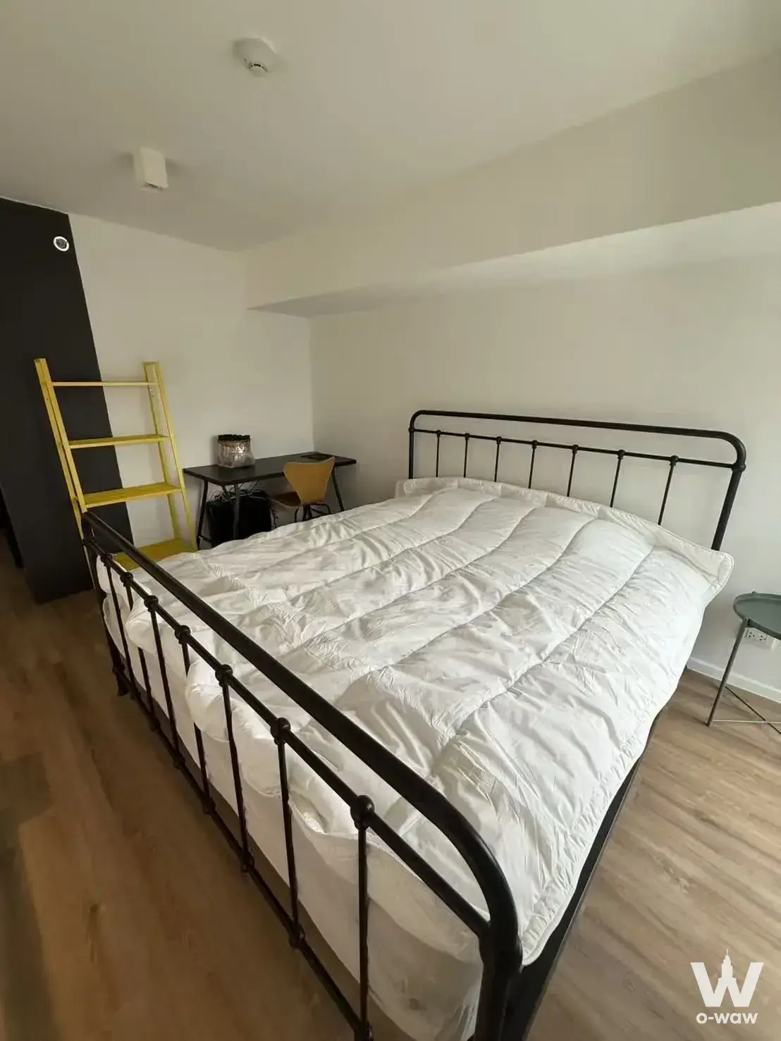 Industrial-style bedroom with black metal bed frame and yellow ladder shelf in The Lofts Silom
