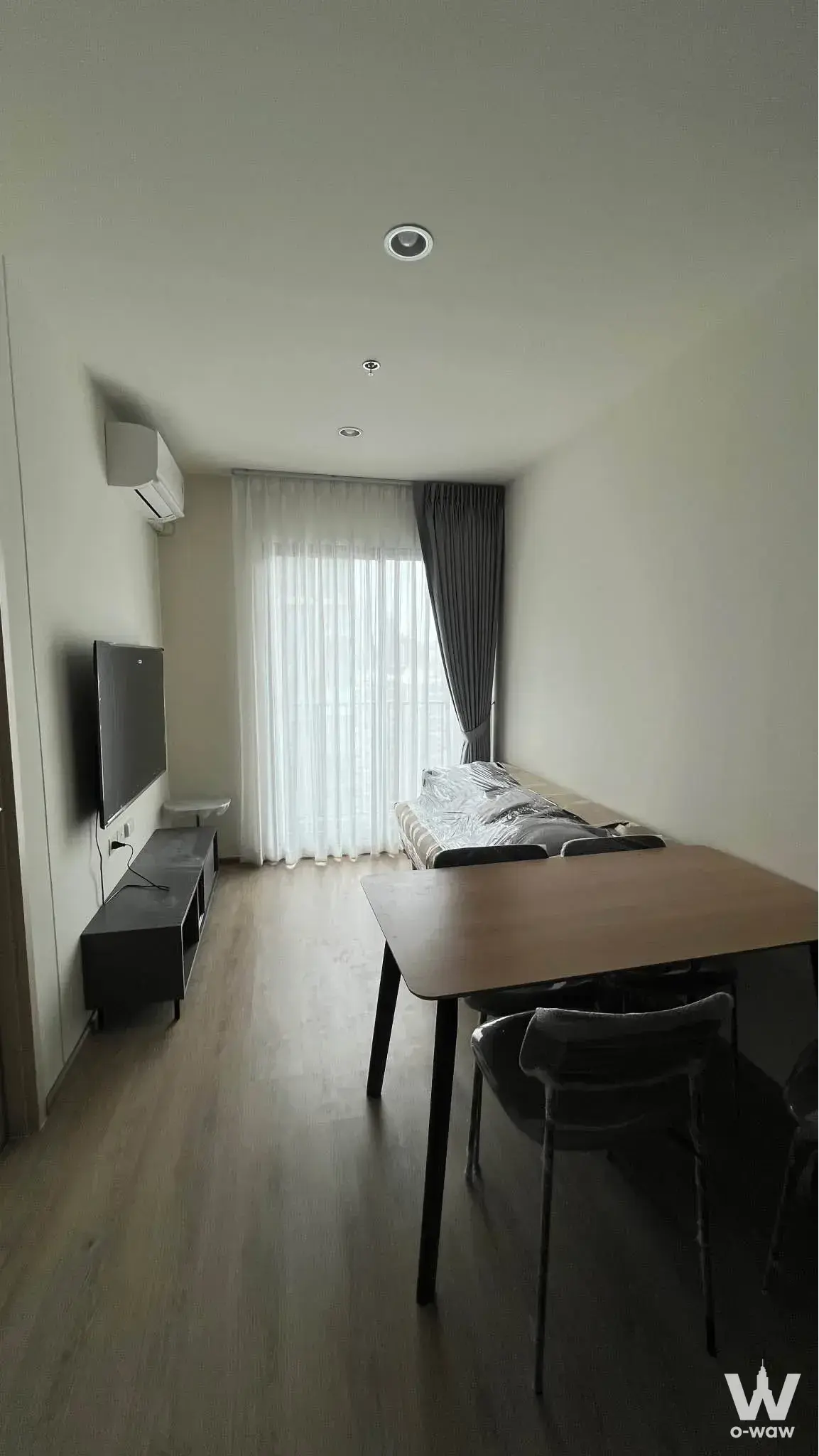 Living room in this Nue District R9 condo with a wall-mounted TV, dining table, and sheer window curtains