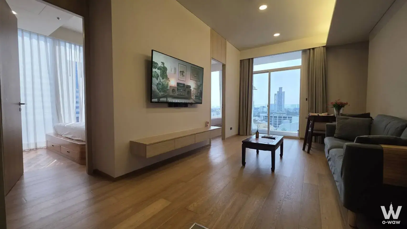 Open living and bedroom in this 2-bed Sukhumvit 42 condo for rent featuring light wood floors and balcony city views
