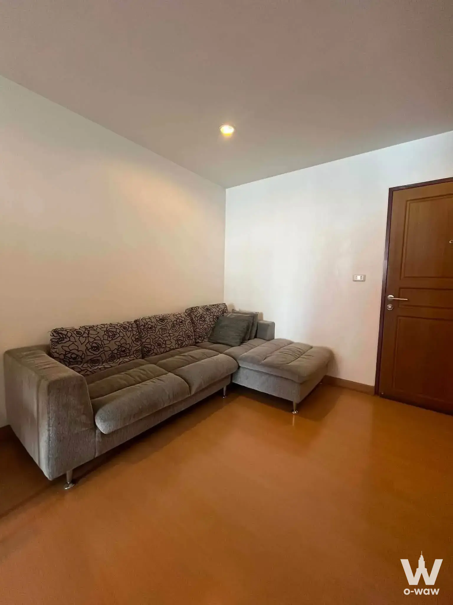 Living room in a 1-bed The Niche Sukhumvit 49 condo with a grey L-shaped sectional sofa and wood floor