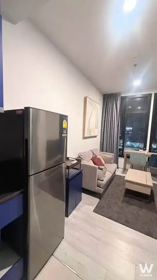 Fully furnished studio living area with beige sofa, blue shelving, and floor-to-ceiling windows overlooking city lights
