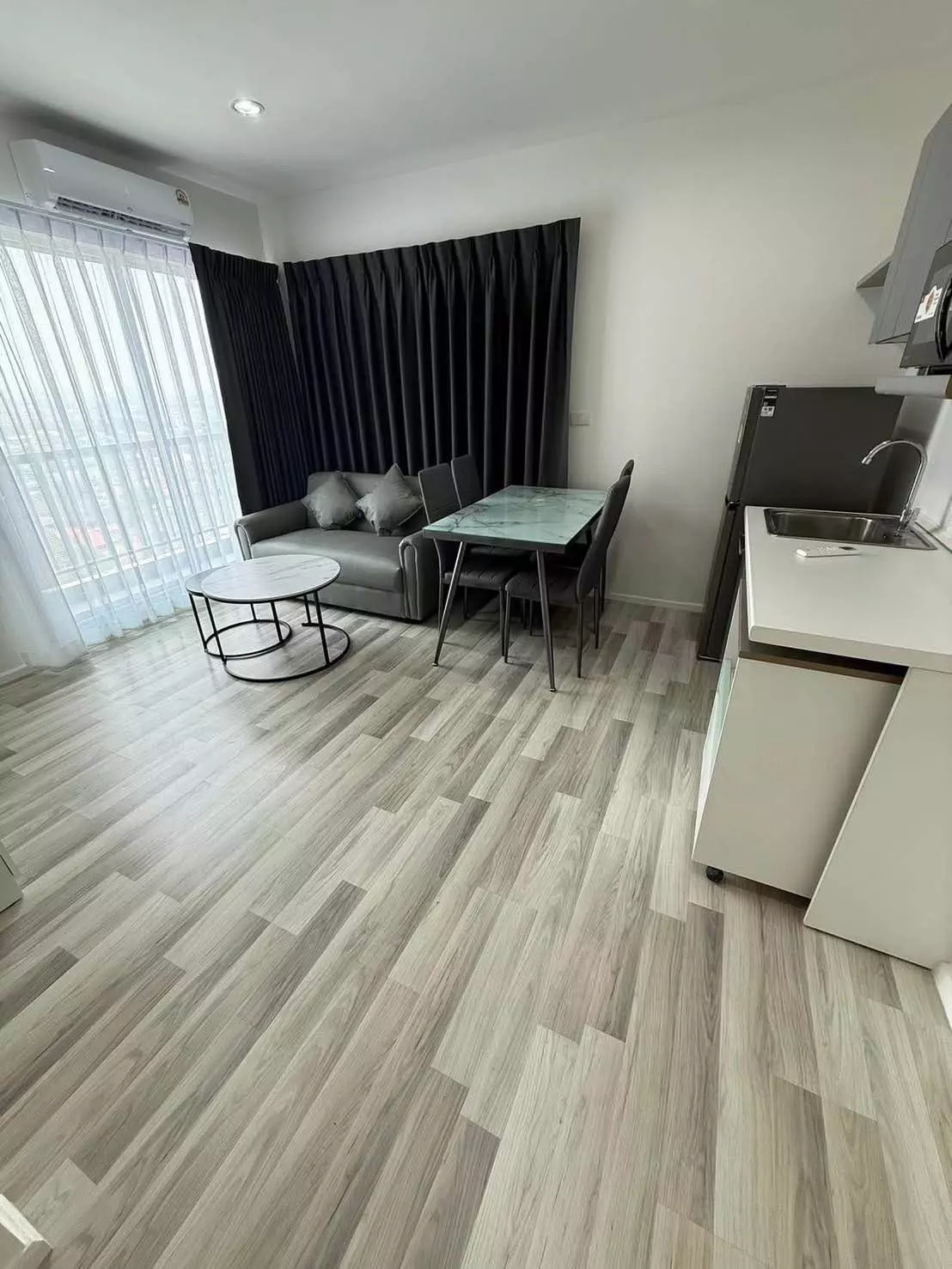 Living area in The Key Cheangwattana featuring grey sofa, marble coffee tables, and green dining table