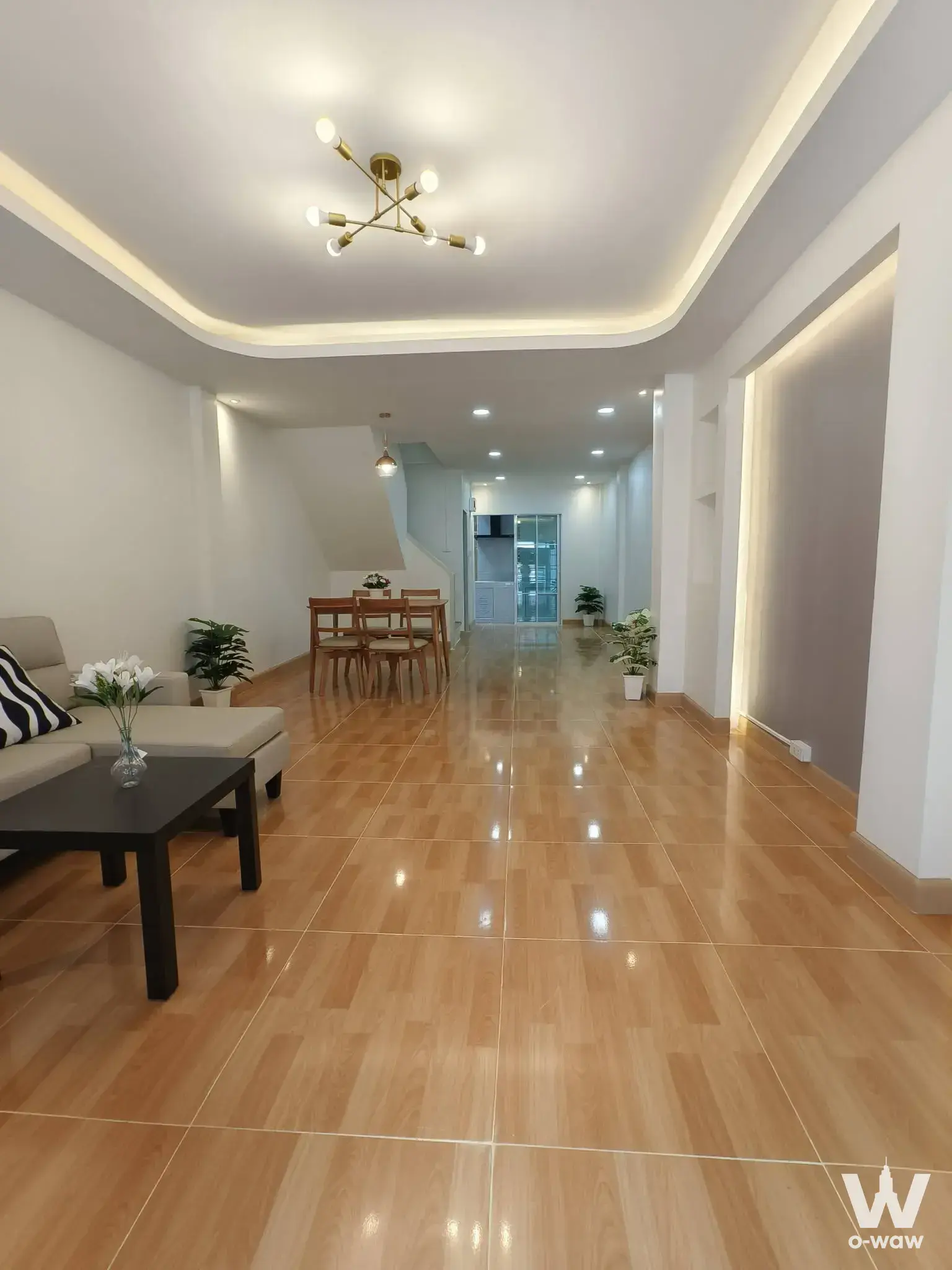 Bright open-plan living and dining area with a beige sectional sofa and gold chandelier in this 3-bed Arden House condo