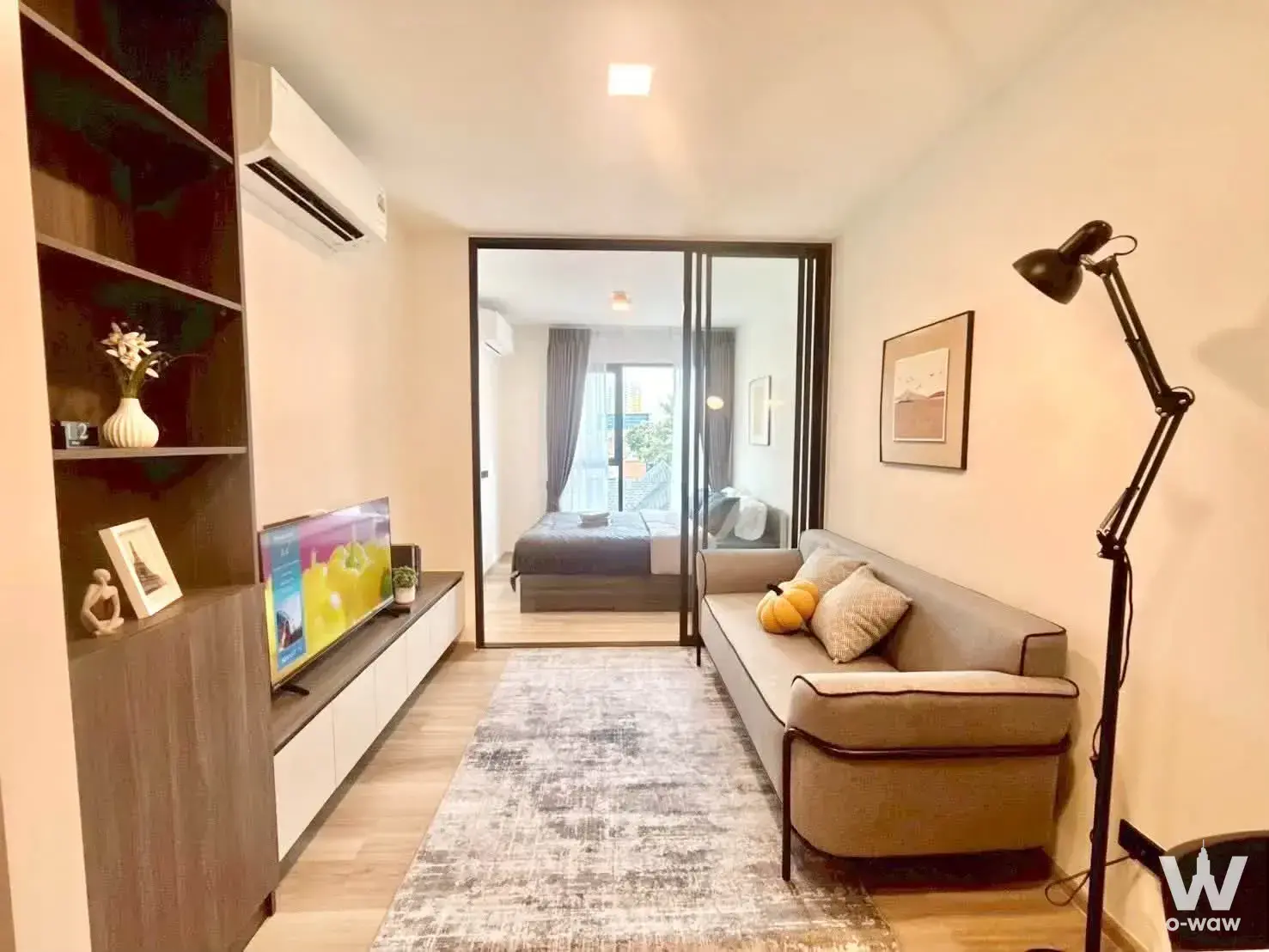 Open-plan studio in CHAPTER ONE MORE KASET condo with grey sofa, built-in shelving, and glass-partitioned bedroom