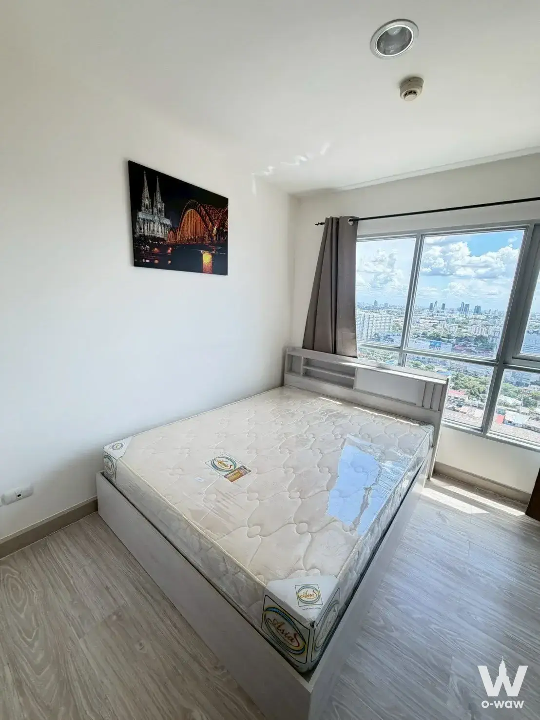 Queen bed with plastic wrap and city view in 1-bed condo for sale at Aspire Ngamwongwan