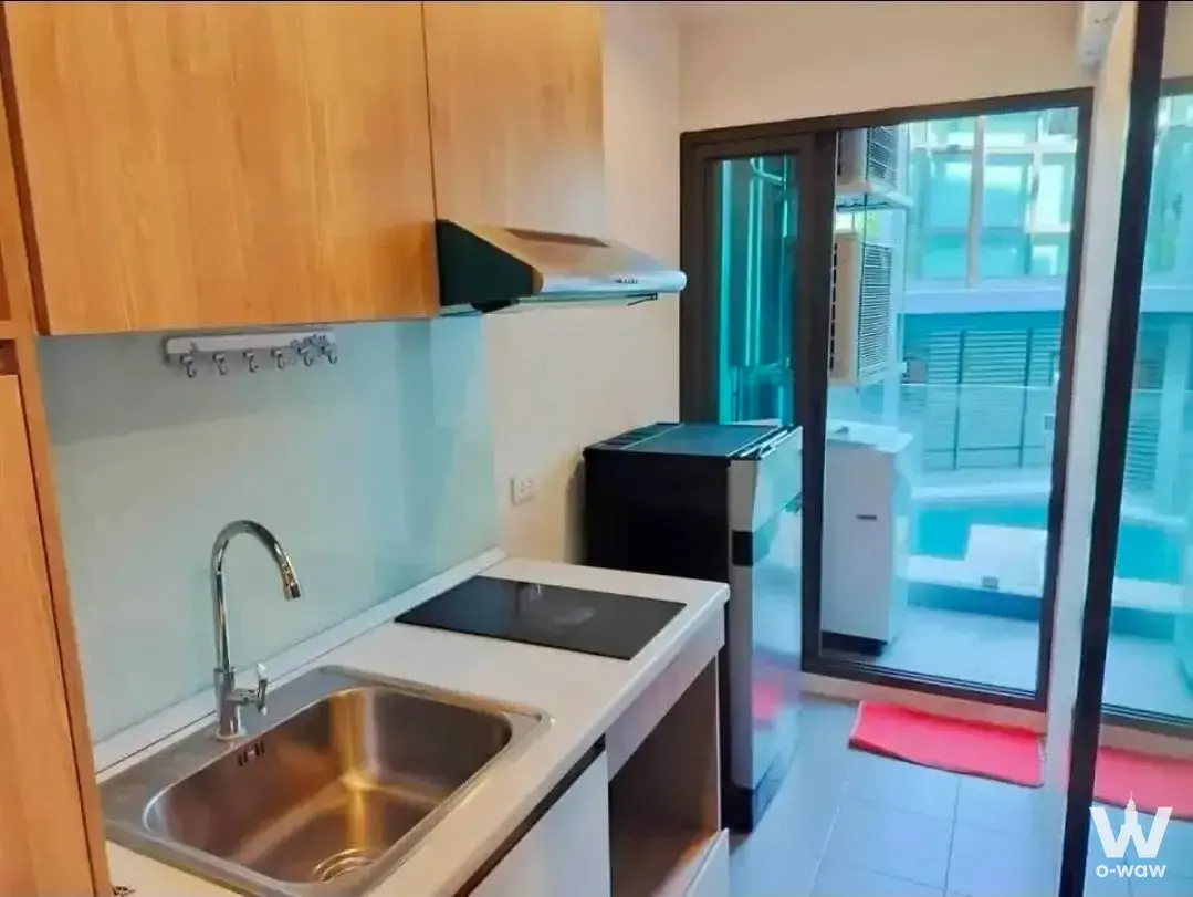 Compact kitchenette in The Excel Hideaway Sukhumvit 50 with white cabinets, induction cooktop, and balcony access