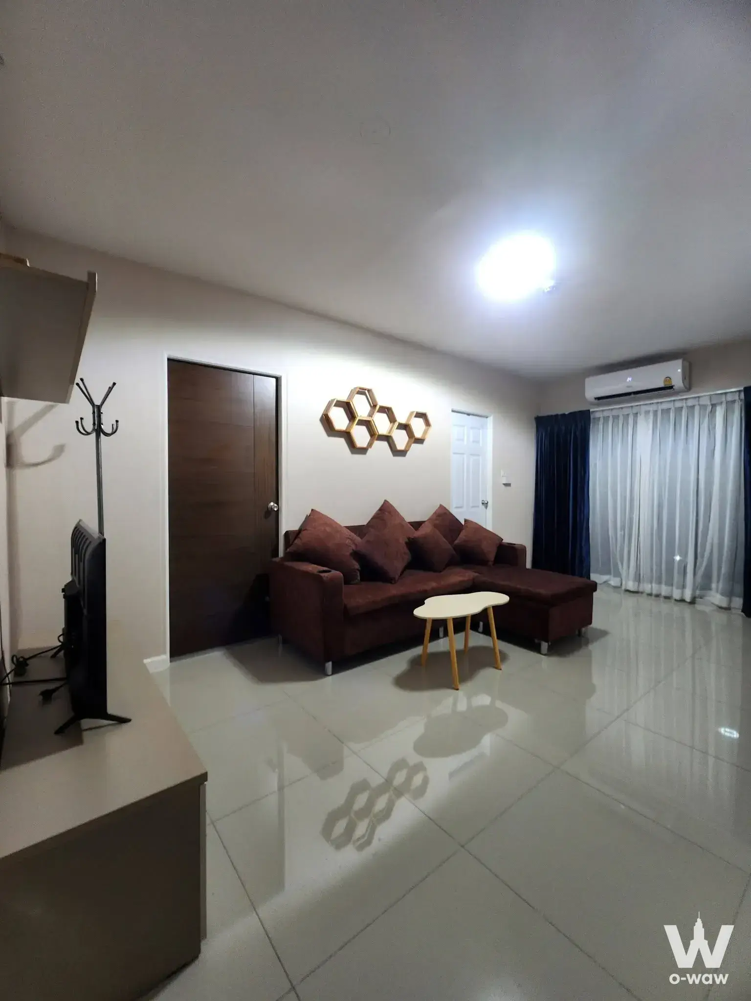 Living room with dark brown sectional sofa and honeycomb wall art in The Privé Ratchada 30