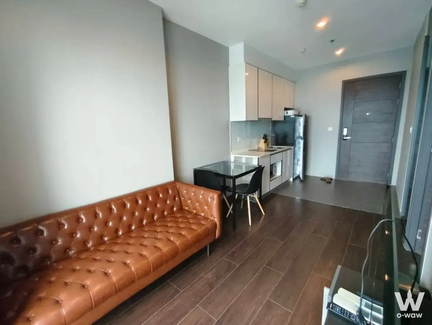 Semi-furnished living room and kitchenette in C Ekkamai Condominium with brown leather Chesterfield sofa